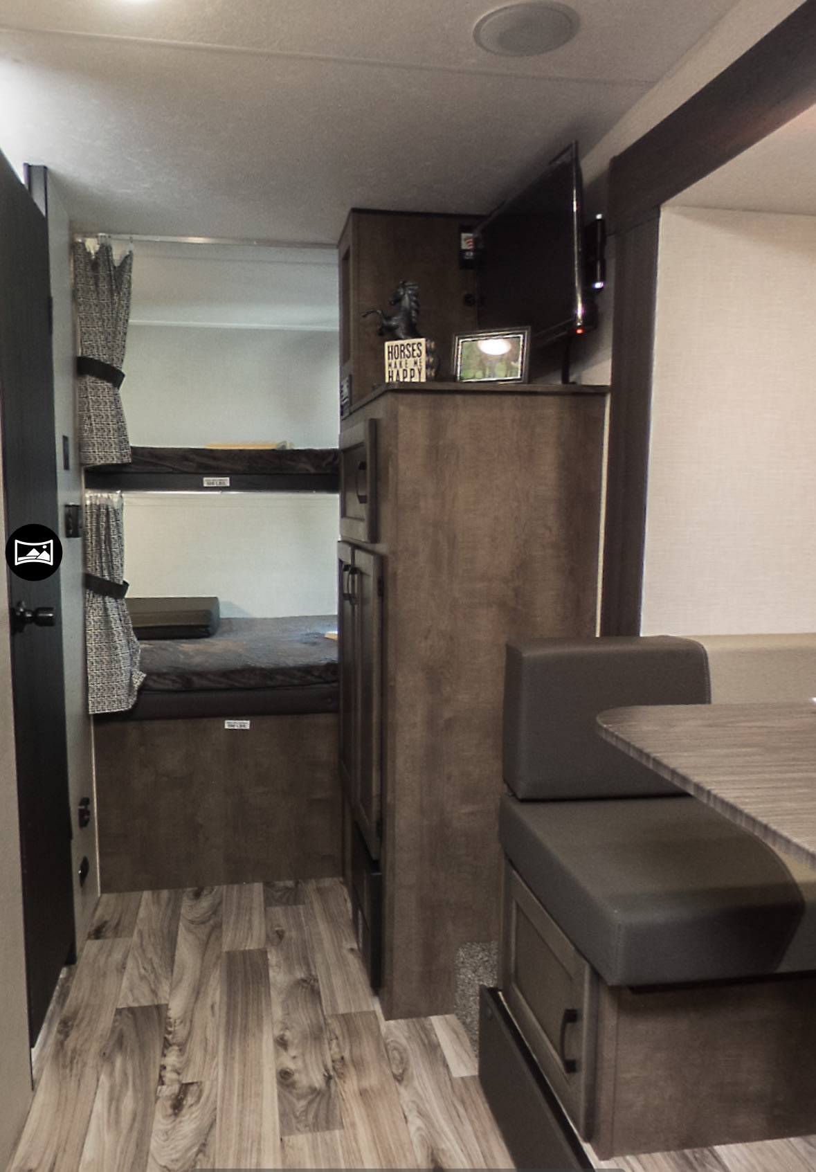 RV rental interior featuring bunk beds with curtains, a mounted TV, and a dinette area with wood-look flooring.. Venture Sonic 2024