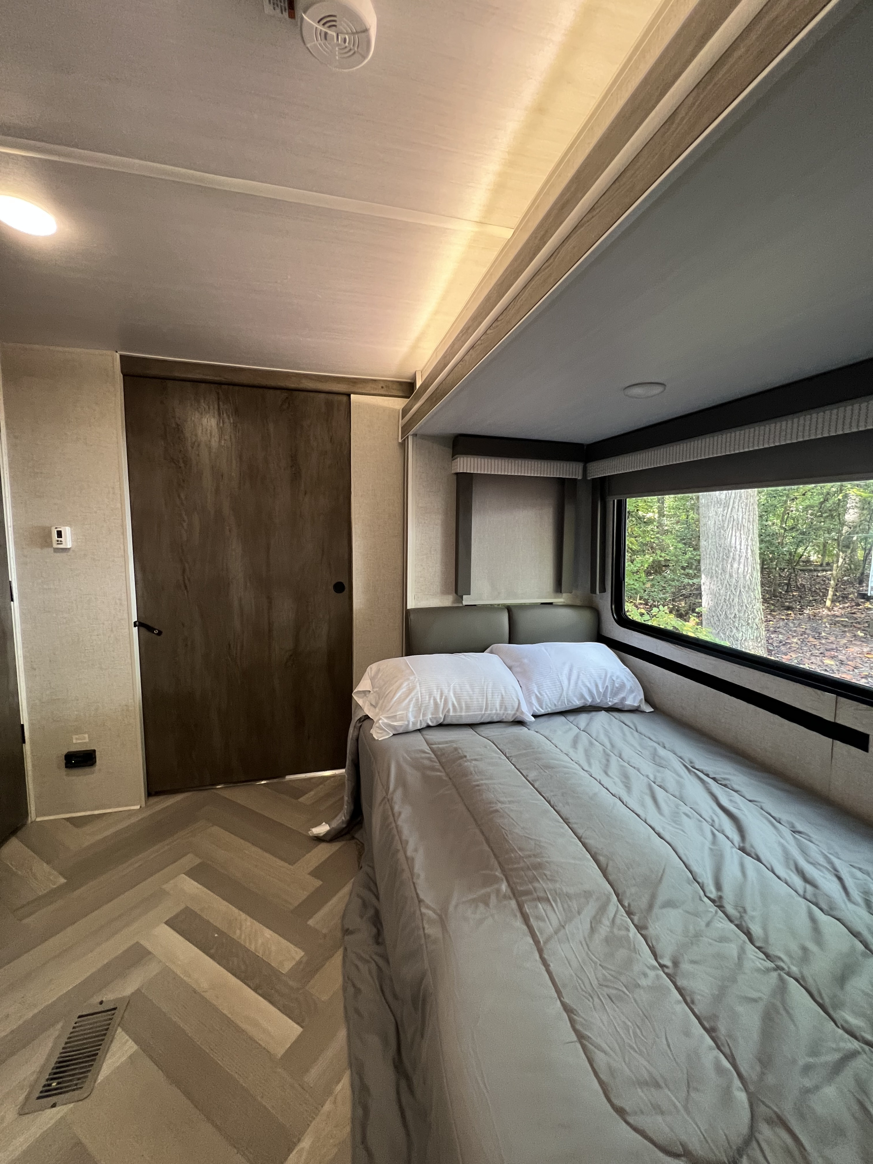 Cozy RV rental bedroom featuring a comfortable bed, window with nature views, and stylish herringbone flooring.. Forest River Wildwood 2021