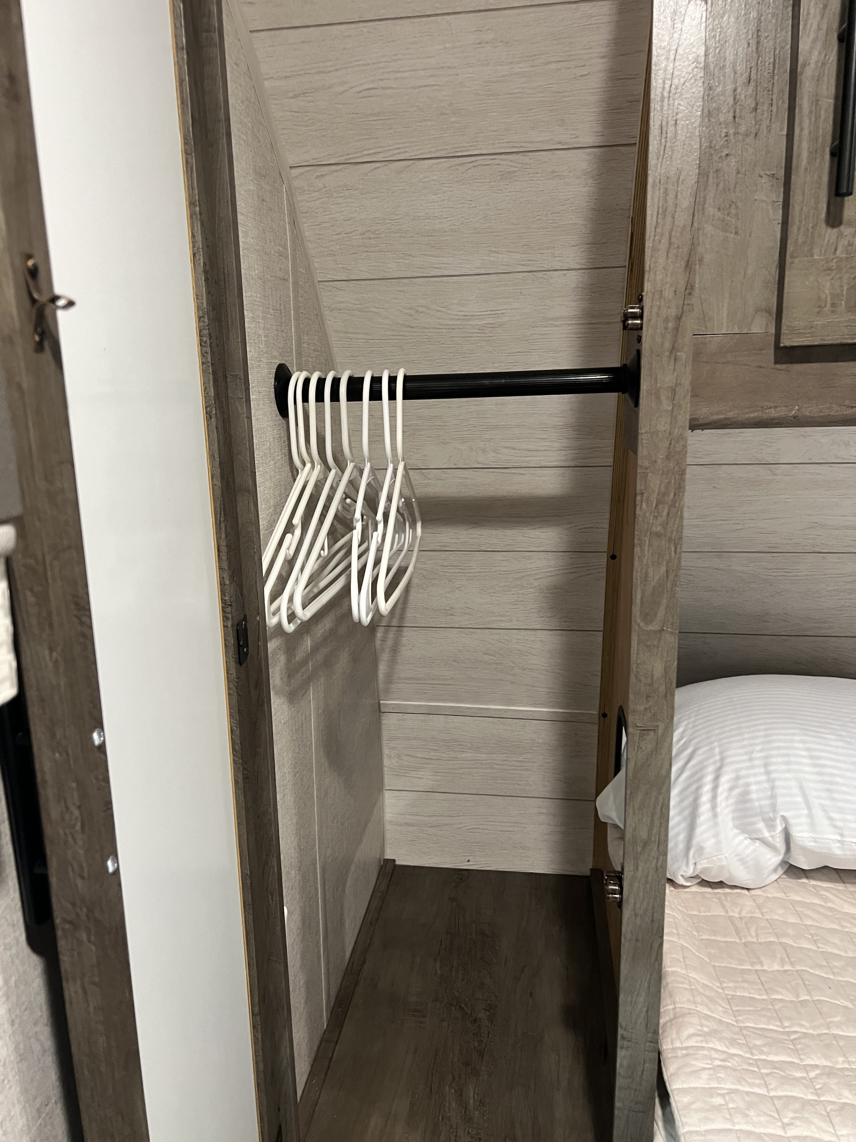 RV rental interior: A compact bedroom closet with empty hangers on a rod, wood-grain walls, and a glimpse of the bed.. Forest River Wildwood 2021