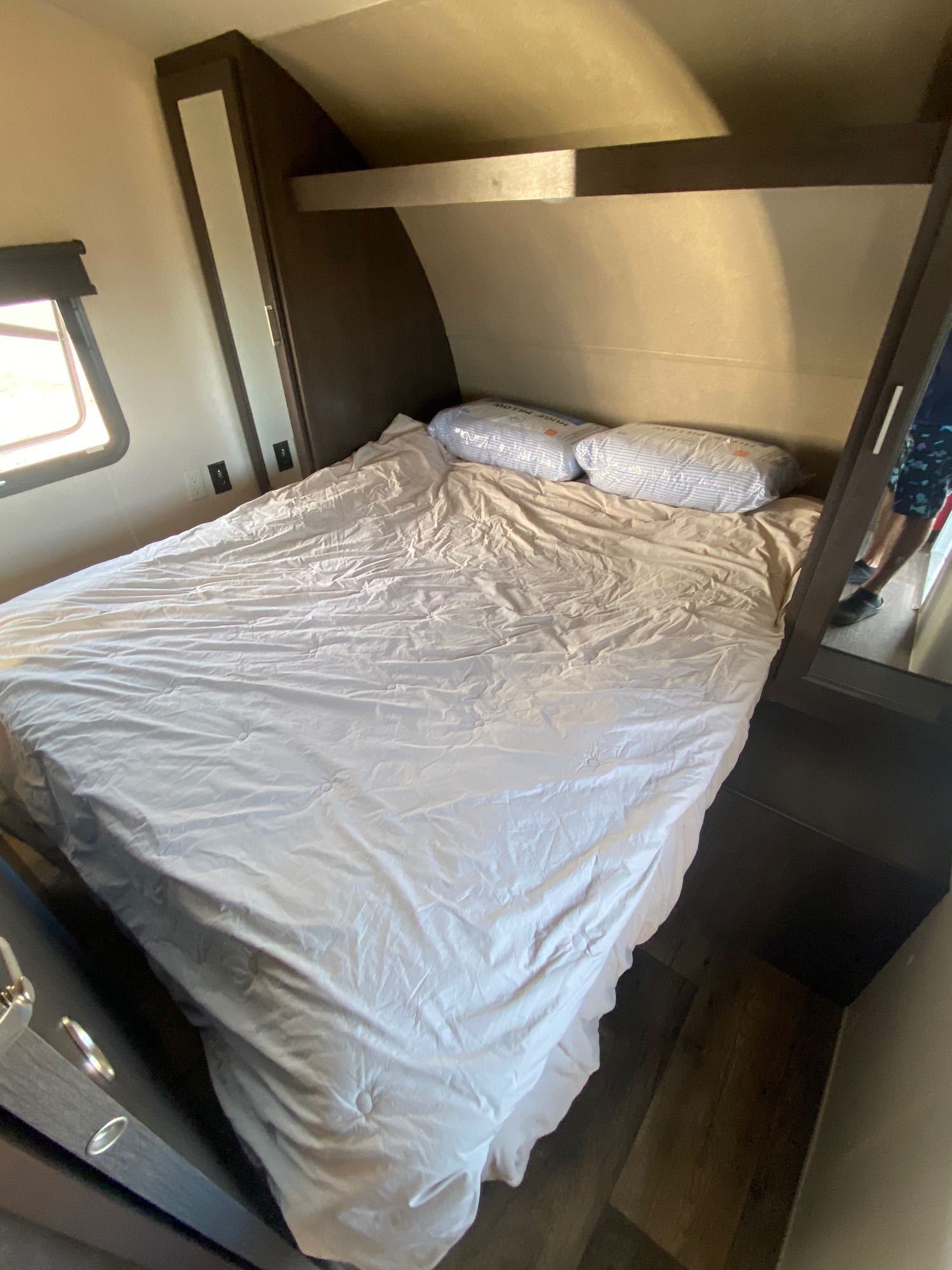 RV rental: view of a compact bedroom with a bed, two pillows, mirrored wardrobe, overhead shelf, and window.. Forest River Wildwood X-Lite 2018