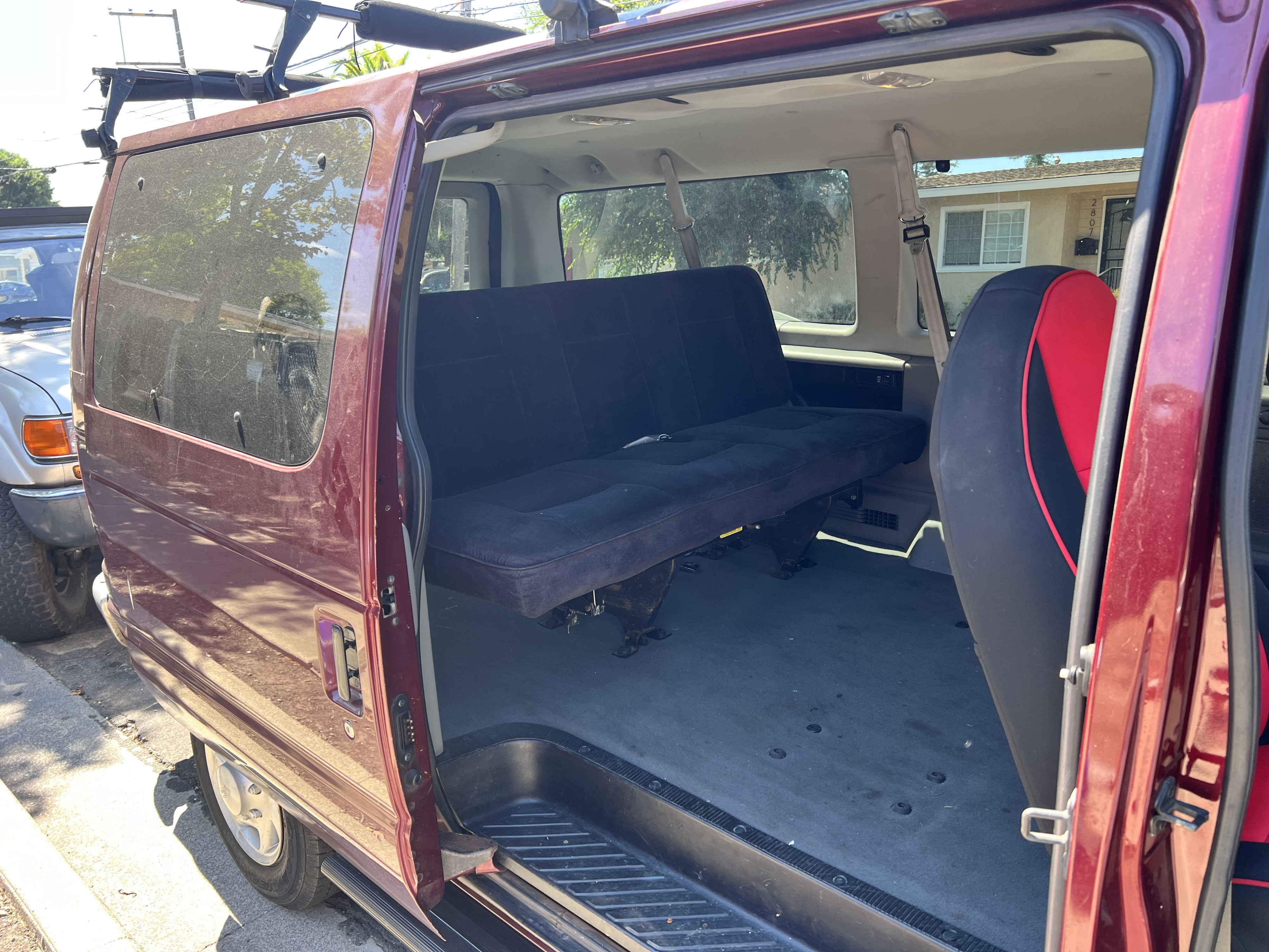 Spacious maroon van interior with open side door, featuring a black convertible bench seat, ideal for rv rental adventures.. Ford Econoline 2006