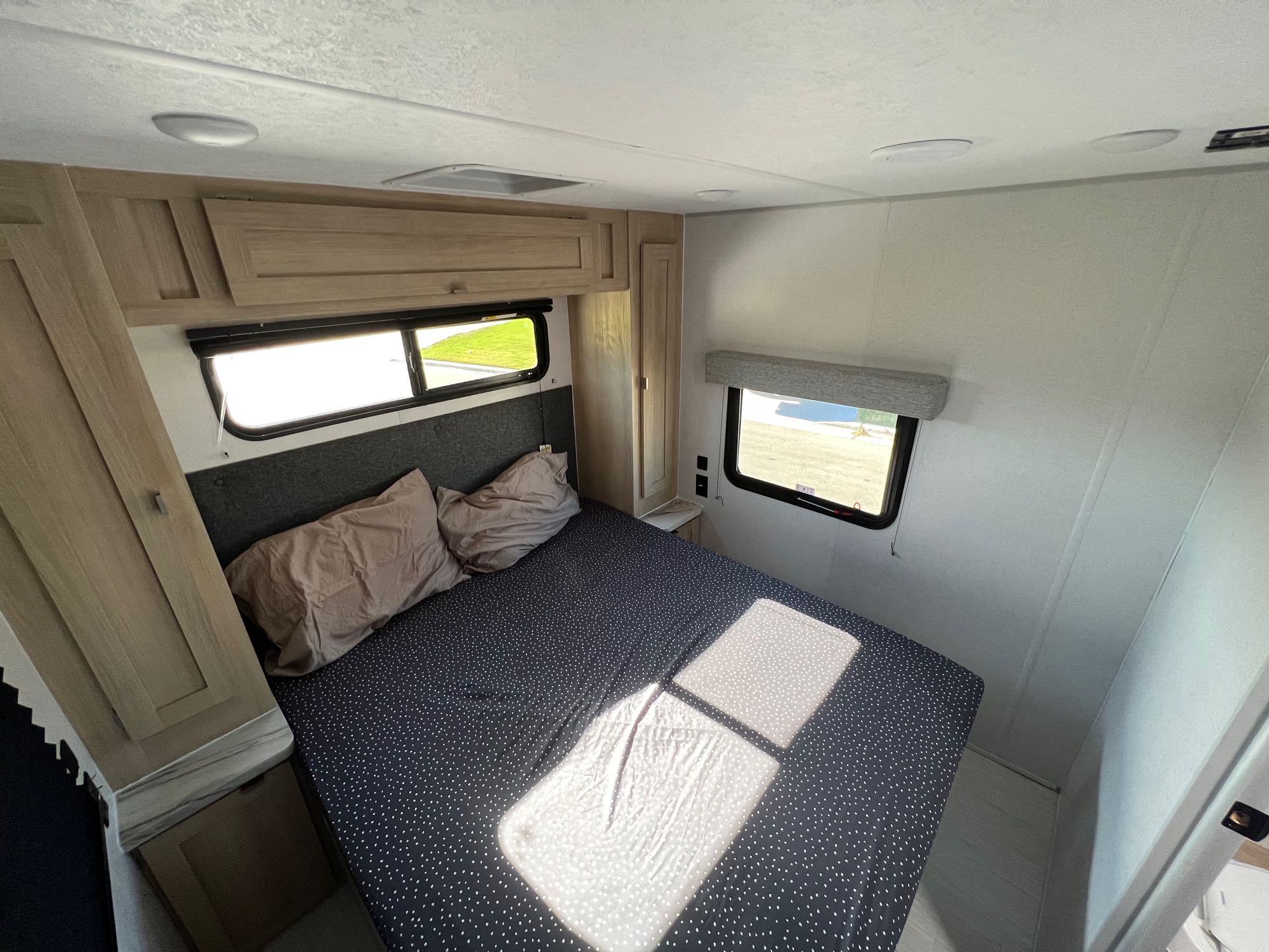 Inside an RV rental, this compact bedroom features a cozy bed with polka dots, overhead storage, and windows bringing in light.. Forest River Wildwood FSX Platinum 2023