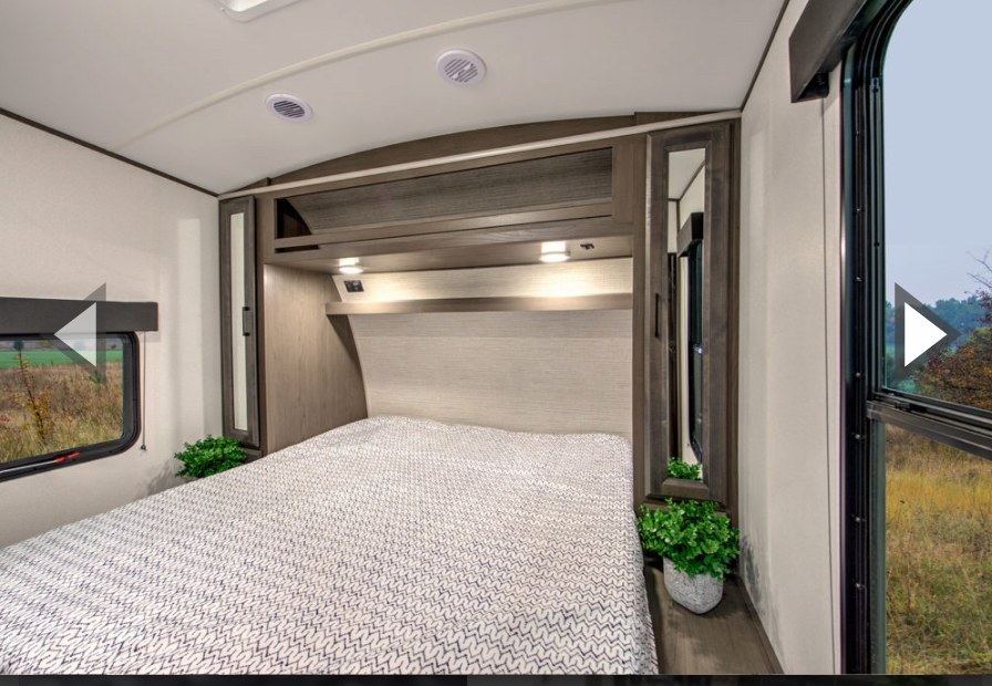 Enjoy comfort in this RV rental bedroom: a spacious bed, overhead storage, mirrored cabinets, and windows overlooking nature.. Heartland Fuel F-265 2022