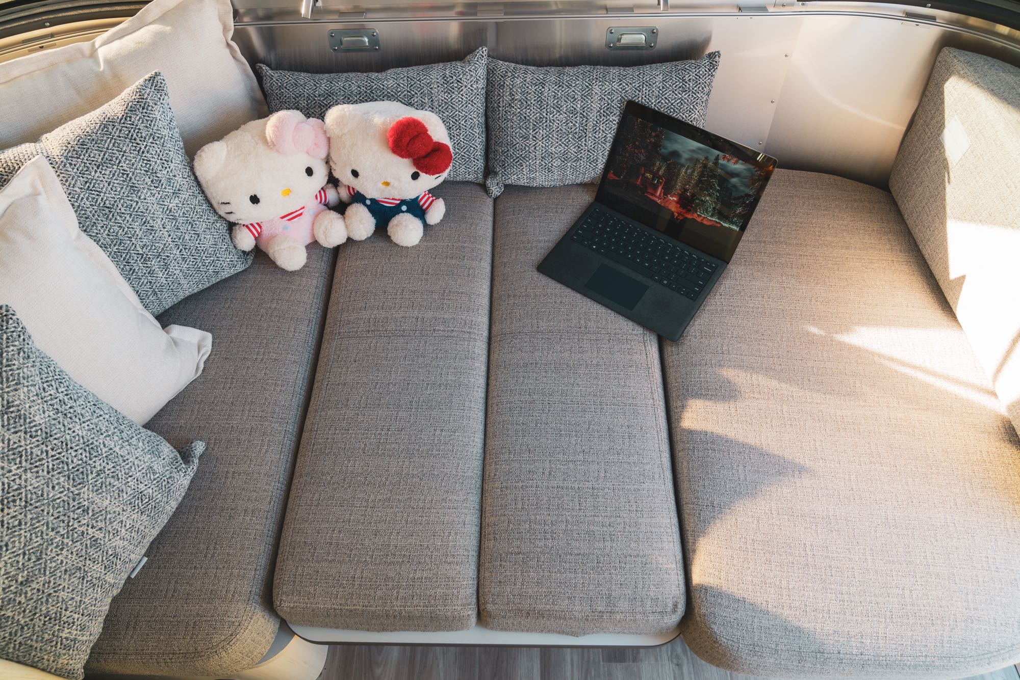 RV rental interior: Comfortable seating, two Hello Kitty plushies, and a laptop. Enjoy cozy travel comfort.. Airstream Bambi 2023