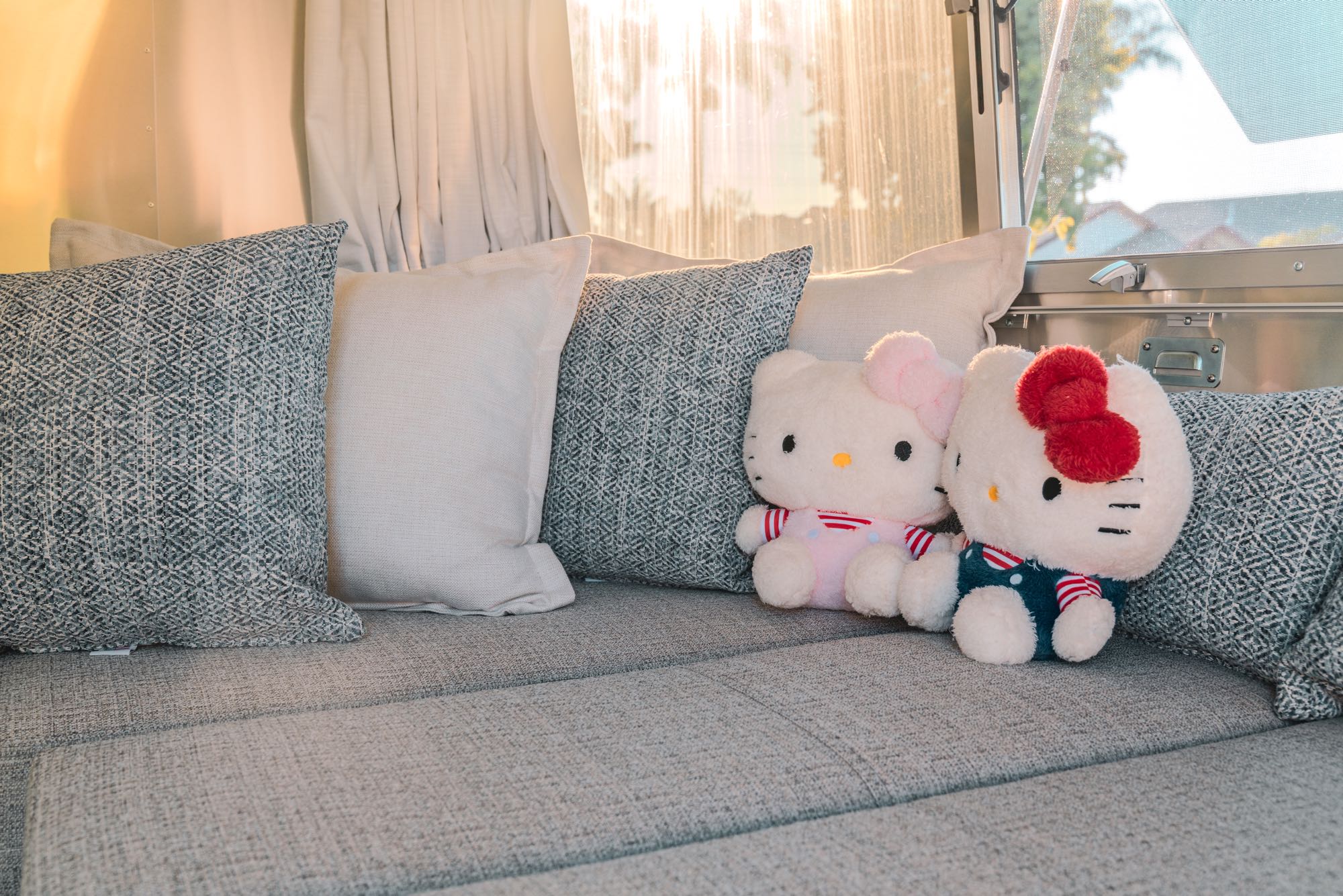 Bright RV rental interior featuring a comfy lounge with stylish pillows and cute Hello Kitty plushies.. Airstream Bambi 2023