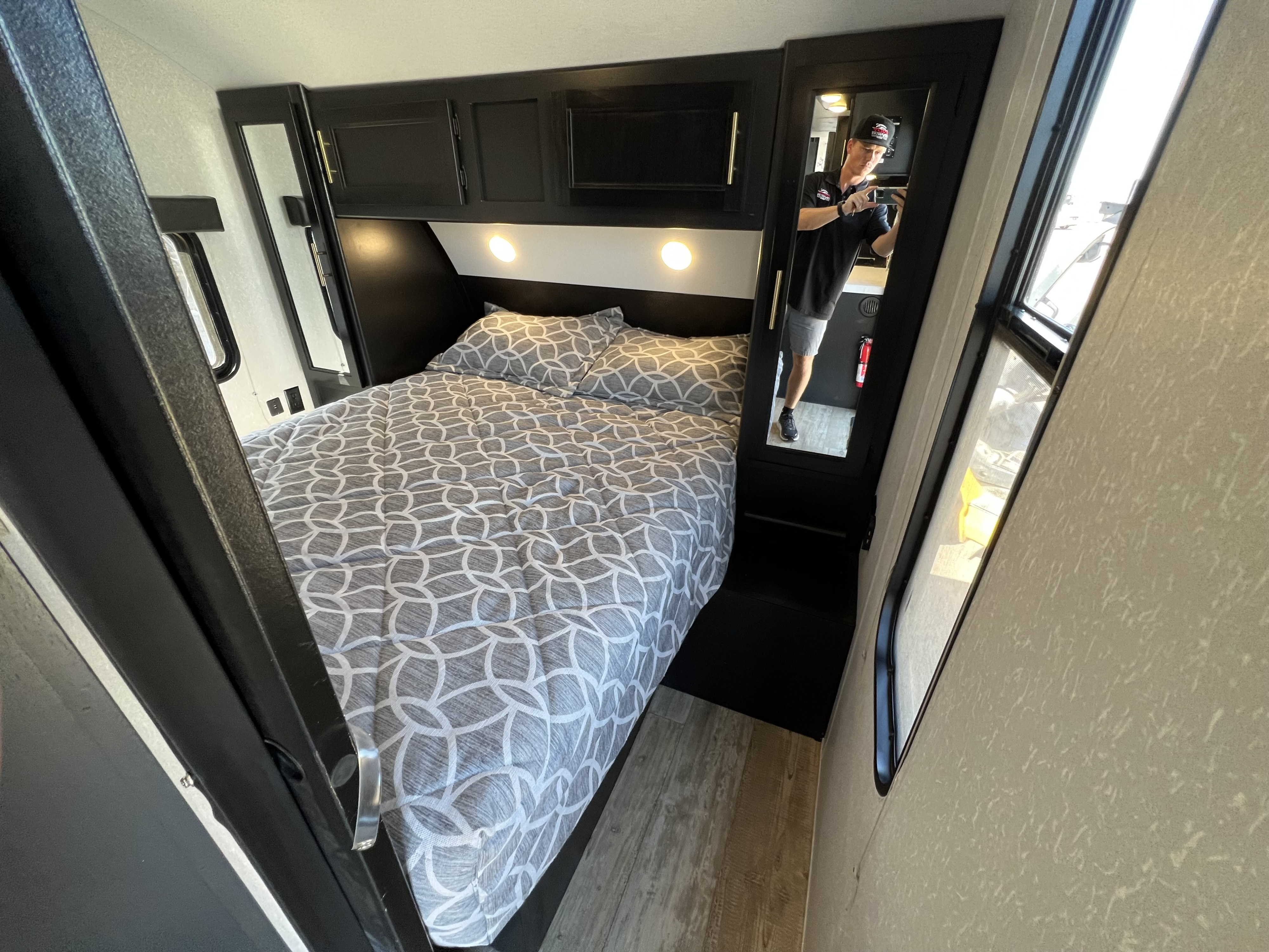 Interior of an RV rental bedroom with a grey patterned bed, dark overhead cabinets, and a tall mirrored door.. Forest River Cherokee Grey Wolf 2020