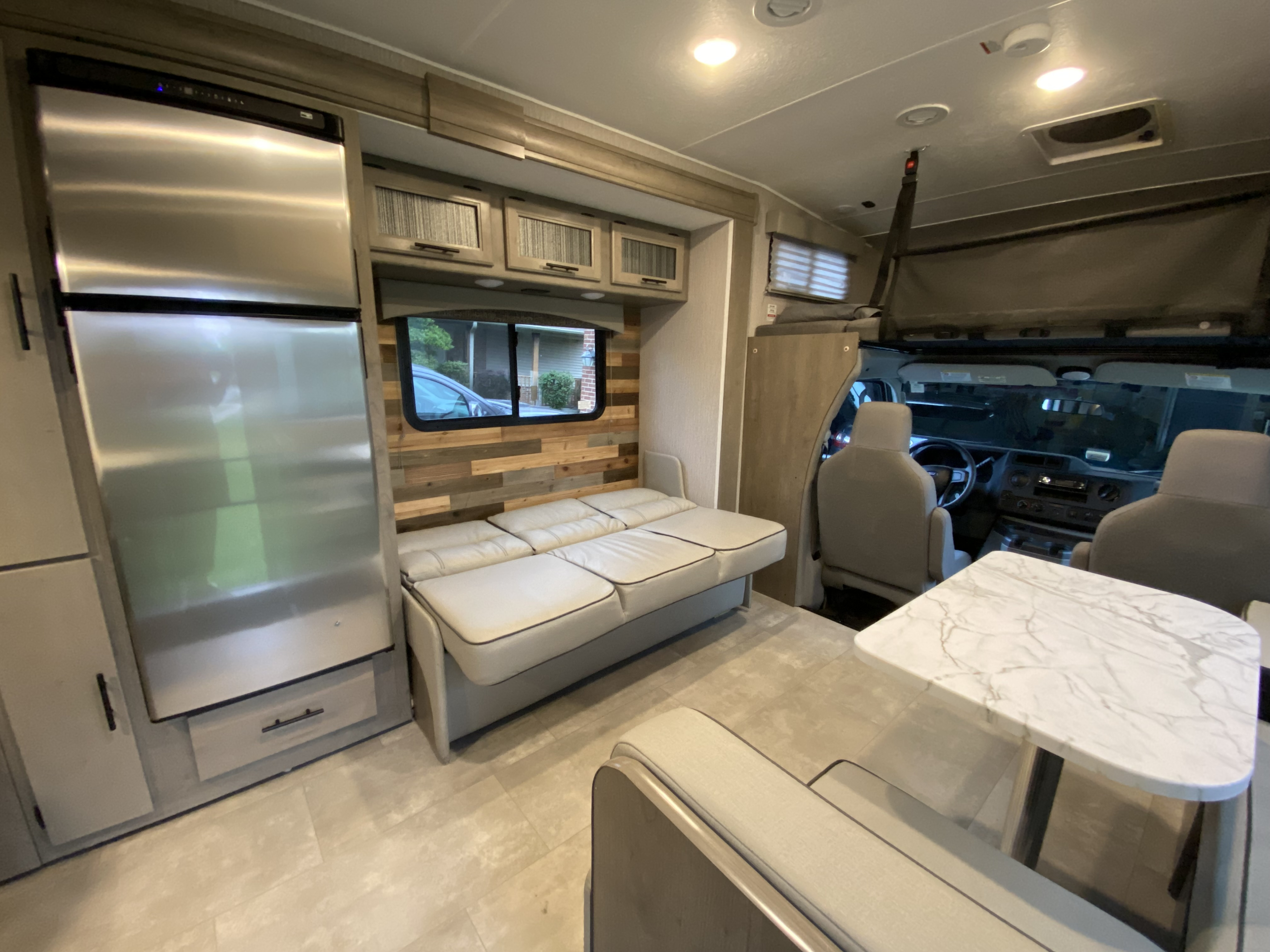 Comfortable RV rental interior: fridge, sofa-bed, wood accent wall, and dining area with a modern table.. Forest River Coachmen Freelander Premier 2022