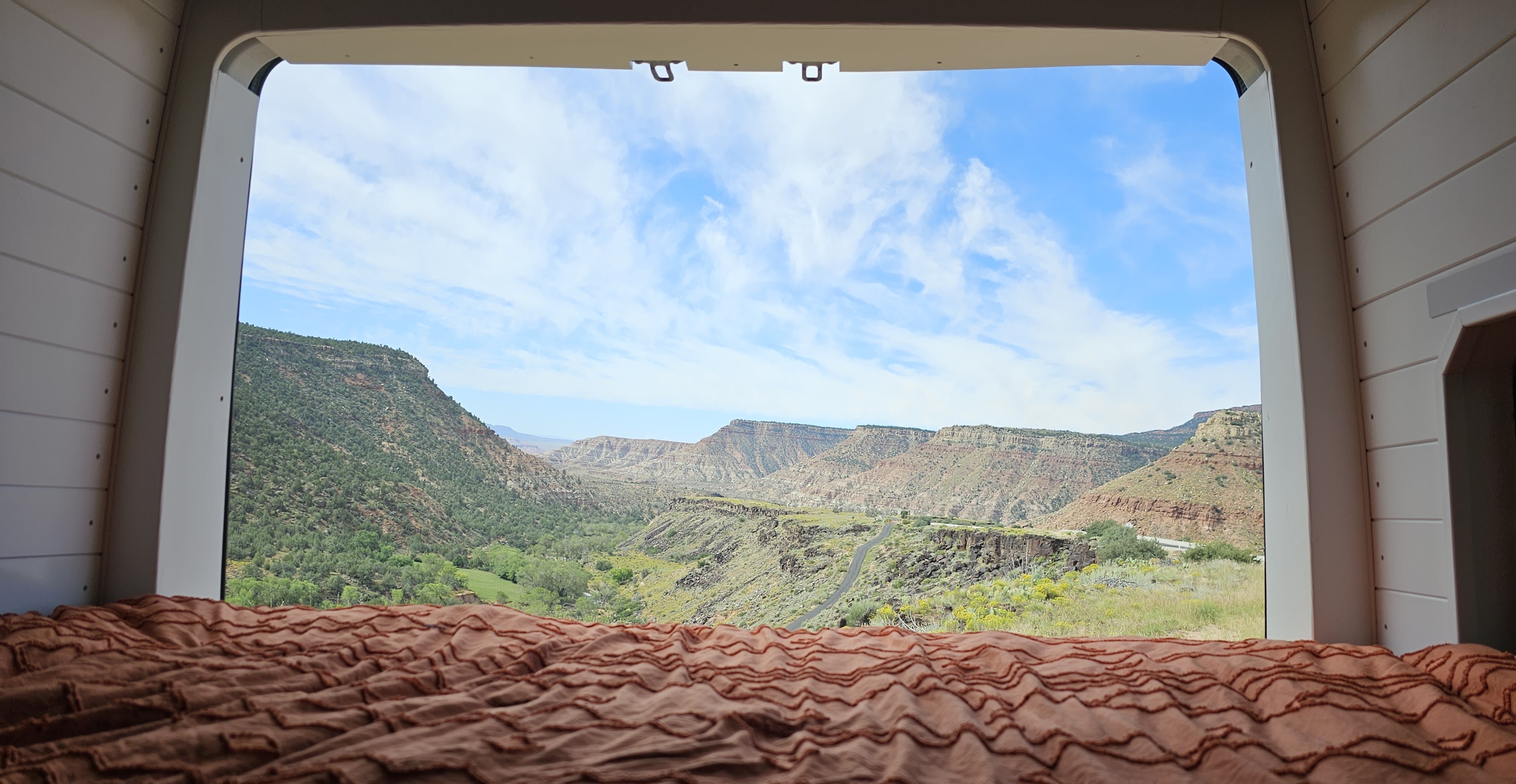 View from an RV rental's bed of a vast, green canyon and distant mountains under a blue sky, ideal for adventurers.. Mercedes-Benz Sprinter 2022