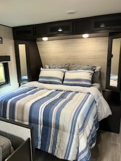 Step inside this cozy RV rental bedroom, featuring a striped bed, overhead storage, and mirrored closets.. Jayco Jay Flight 2022