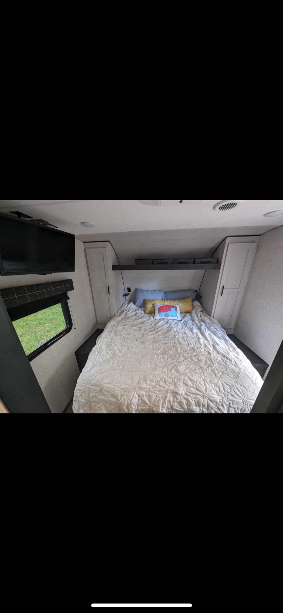 Cozy RV rental bedroom with TV, window view, and smart storage. Features a comfy bed and bright pillows.. Sportsmen SE 2022