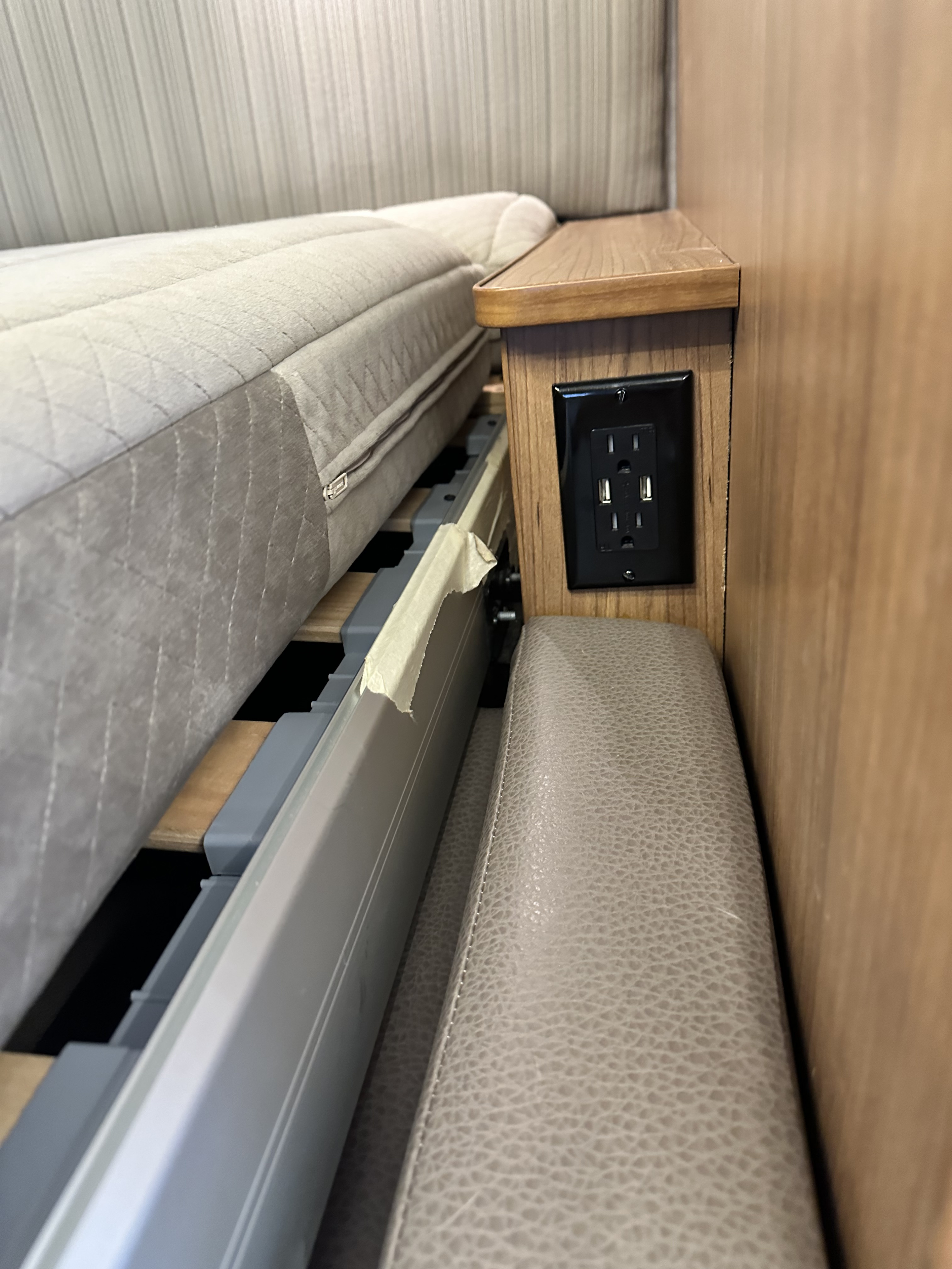 RV rental bed area with integrated USB/AC power outlet, showing mattress and slat system for convenient charging.. Winnebago View 2018