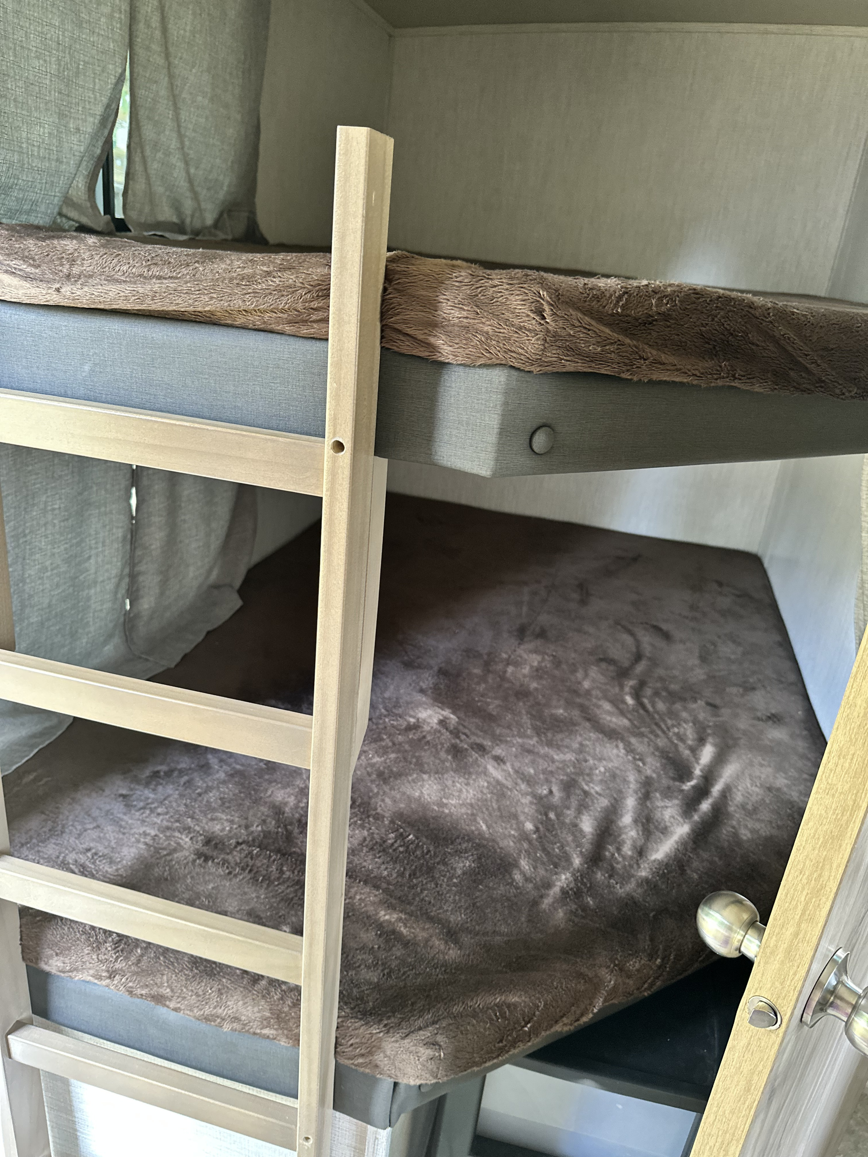 Cozy bunk beds in an RV rental, featuring soft brown blankets and a wooden ladder. Perfect compact sleeping for travel.. Forest River Palomino Solaire 2021