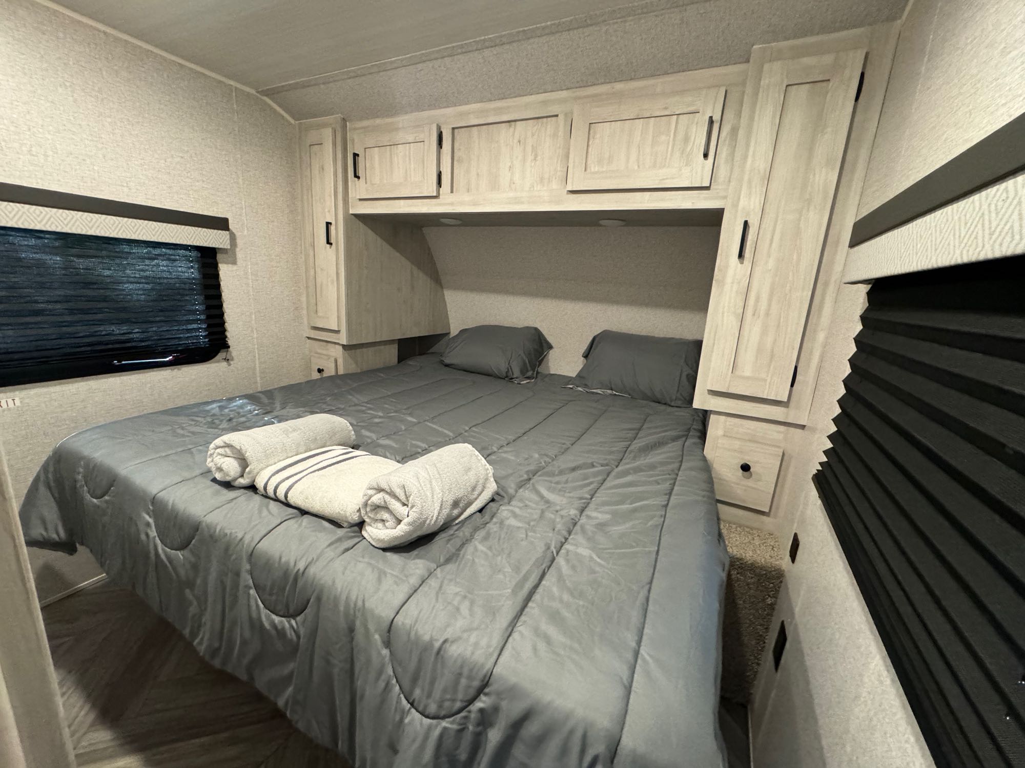 Modern RV rental bedroom featuring a queen bed with fresh towels, overhead cabinets, and blackout blinds for a restful stay.. East to West Della Terra 2022
