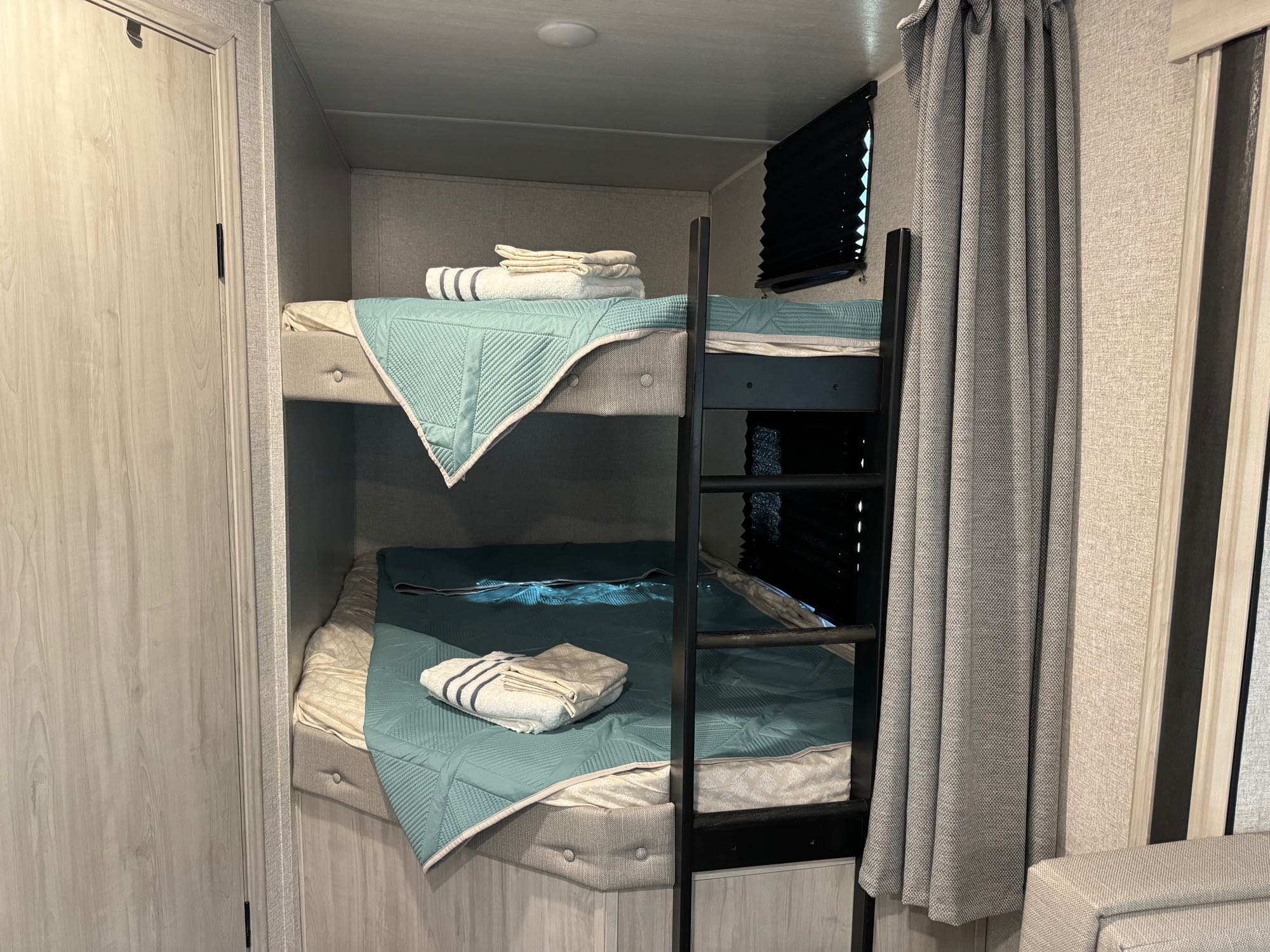 Cozy teal-quilted bunk beds in a modern rv rental, featuring a ladder and light wood accents.. East to West Della Terra 2022