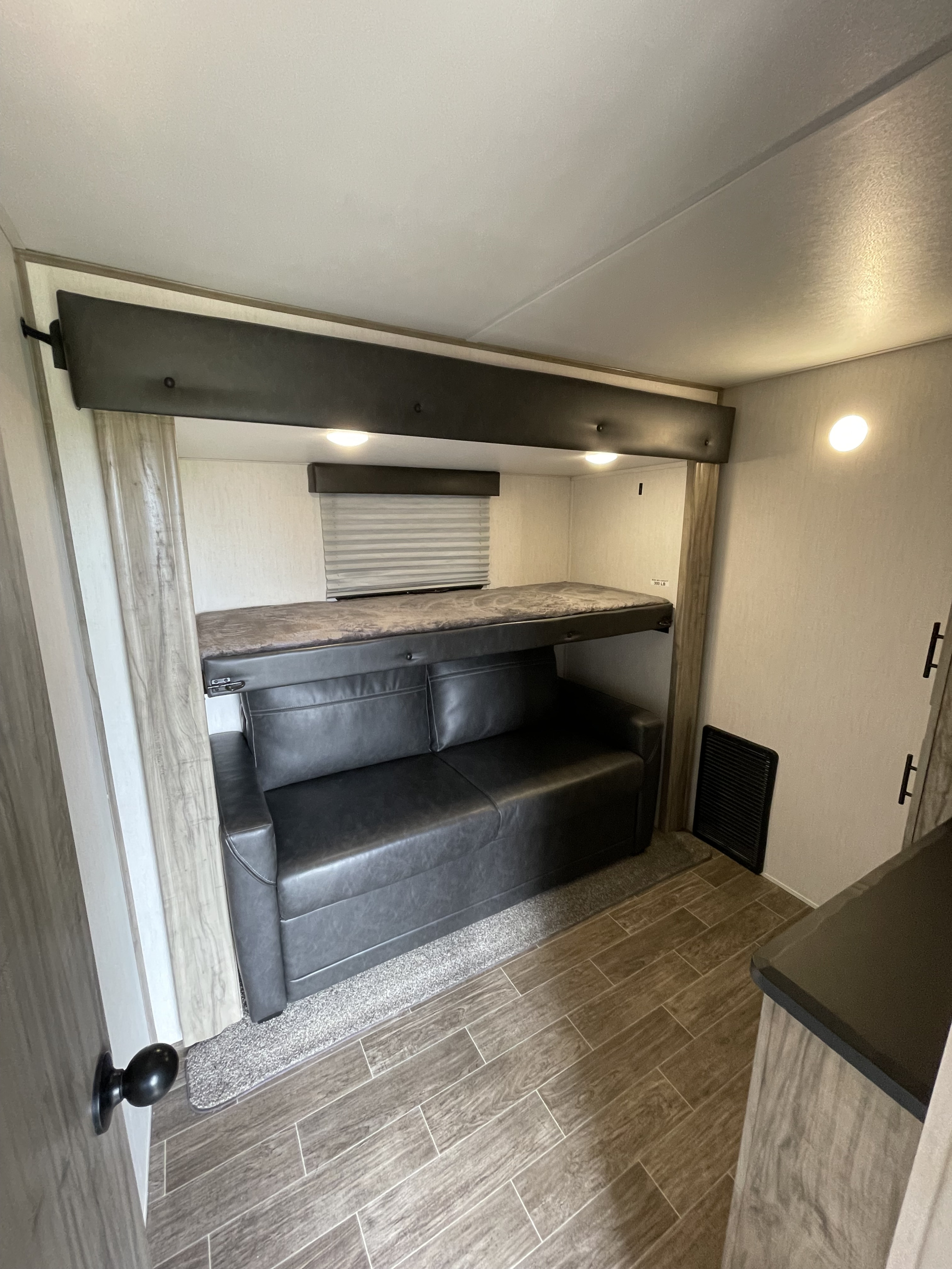 RV rental interior features a convertible sofa below a bunk bed, wood-look flooring, and bright overhead lighting.. Forest River Cherokee Arctic Wolf 2021