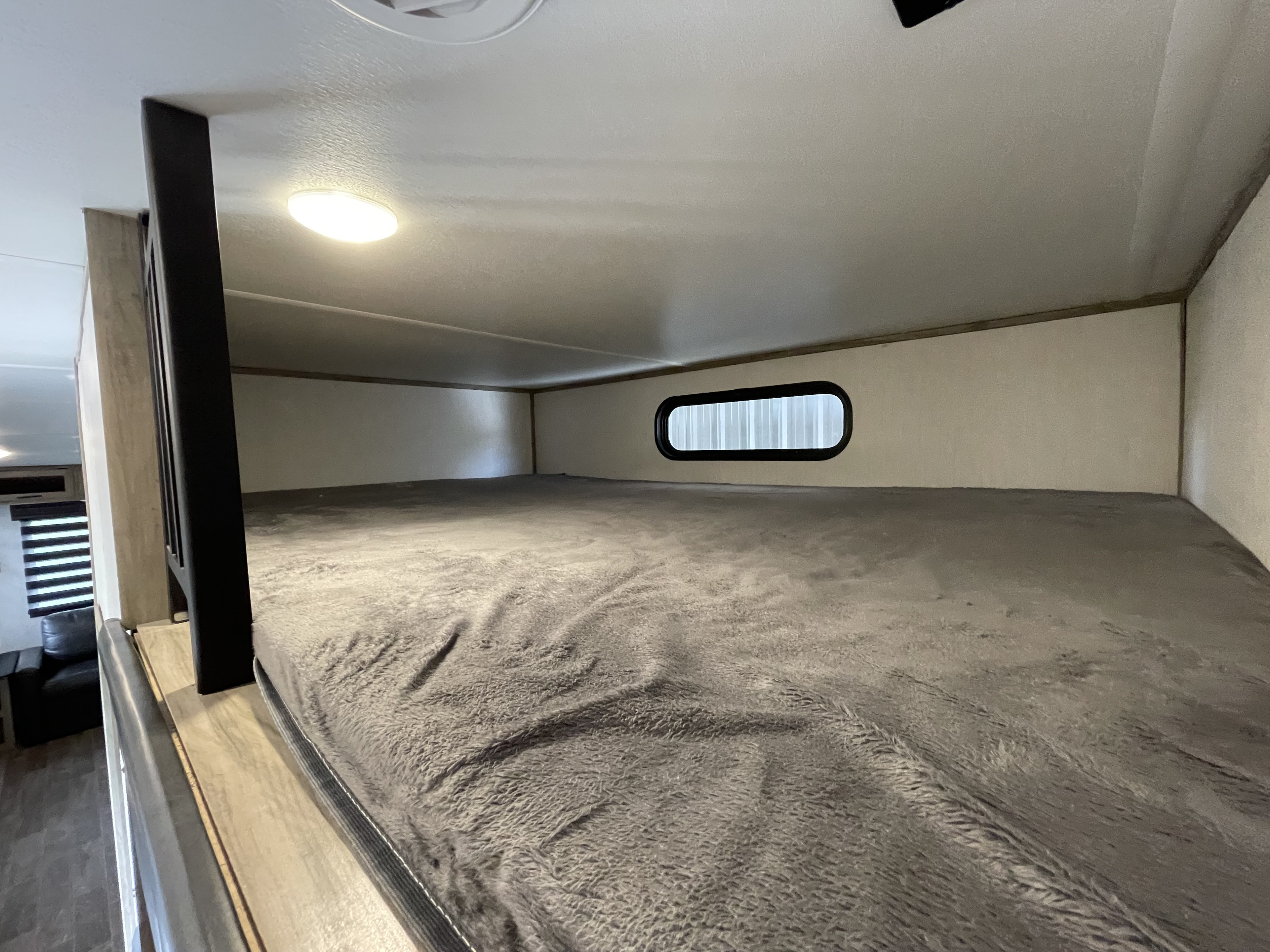 Inside an RV rental: a plush grey bunk bed with a window, offering a comfy sleeping space for your adventure.. Forest River Cherokee Arctic Wolf 2021