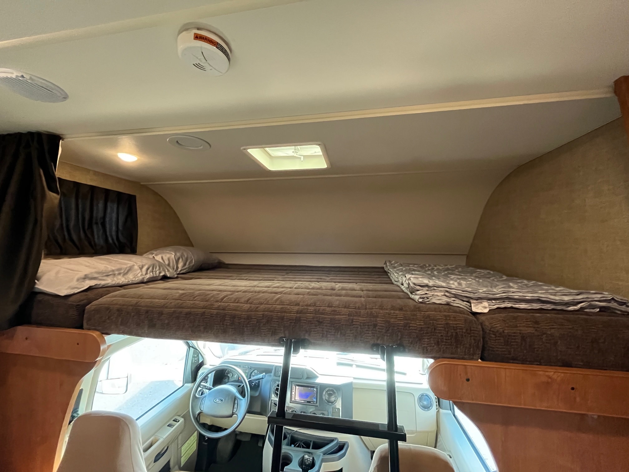 Spacious over-cab bunk bed in an RV rental, showing the cozy sleeping area and driver's cabin below.. Winnebago Minnie Winnie 2017