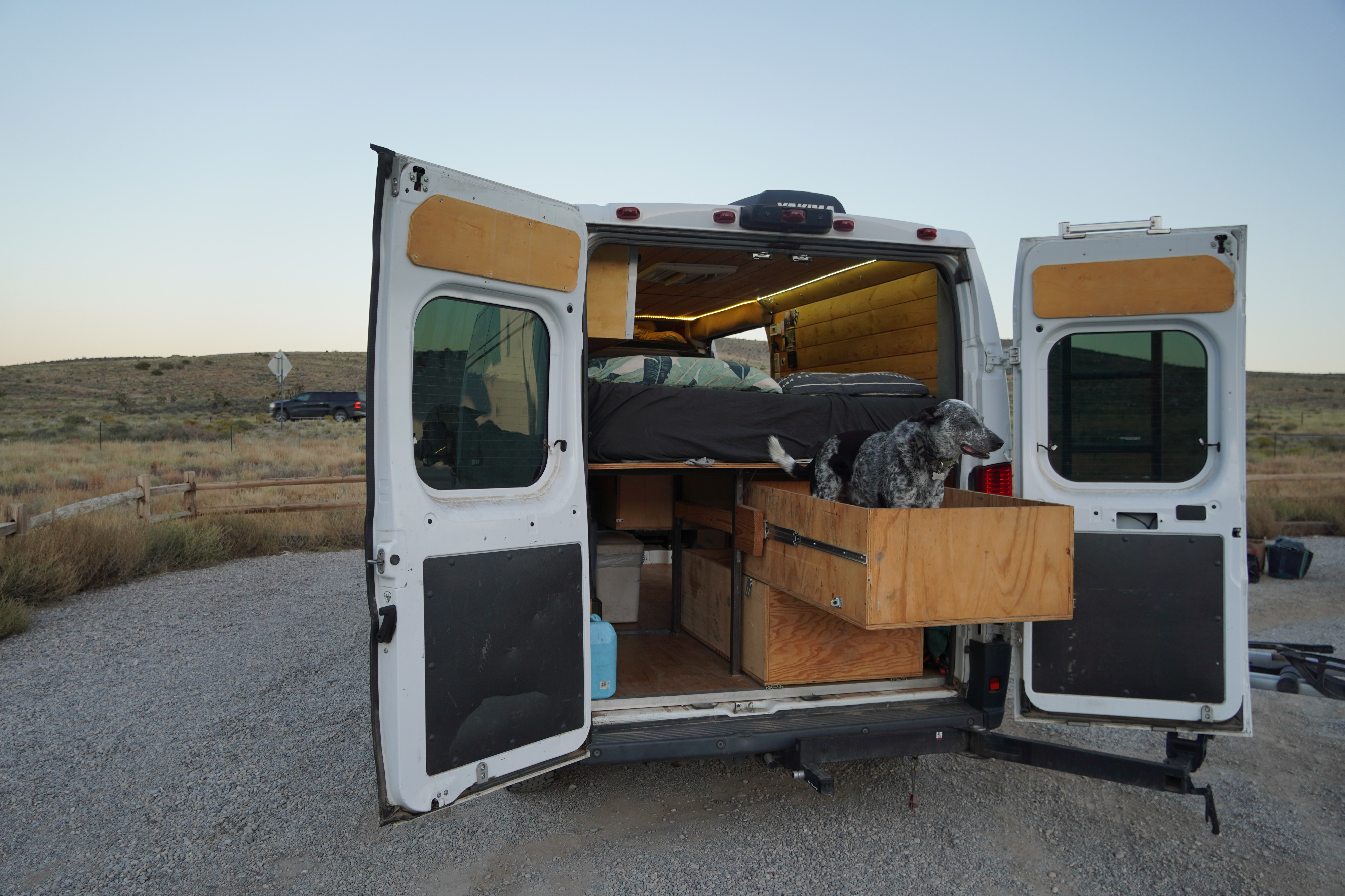 This RV rental features a cozy wooden interior with a bed and a dog in a pull-out drawer, ready for van life adventures.. Dodge Promaster 2500 2017