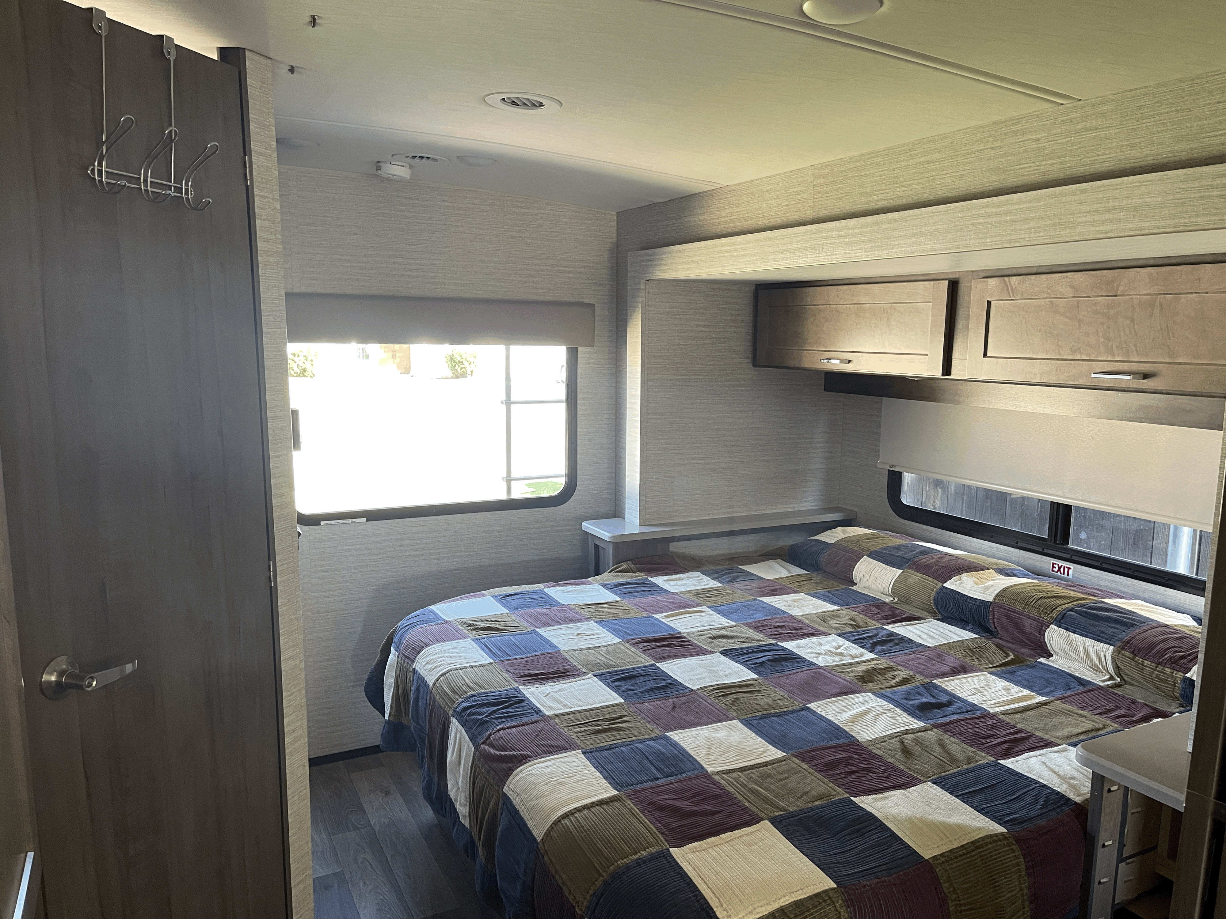 Step into comfort: a cozy RV rental bedroom featuring a patchwork quilt, ample overhead storage, and natural light from a large window.. Winnebago Sunstar 2021
