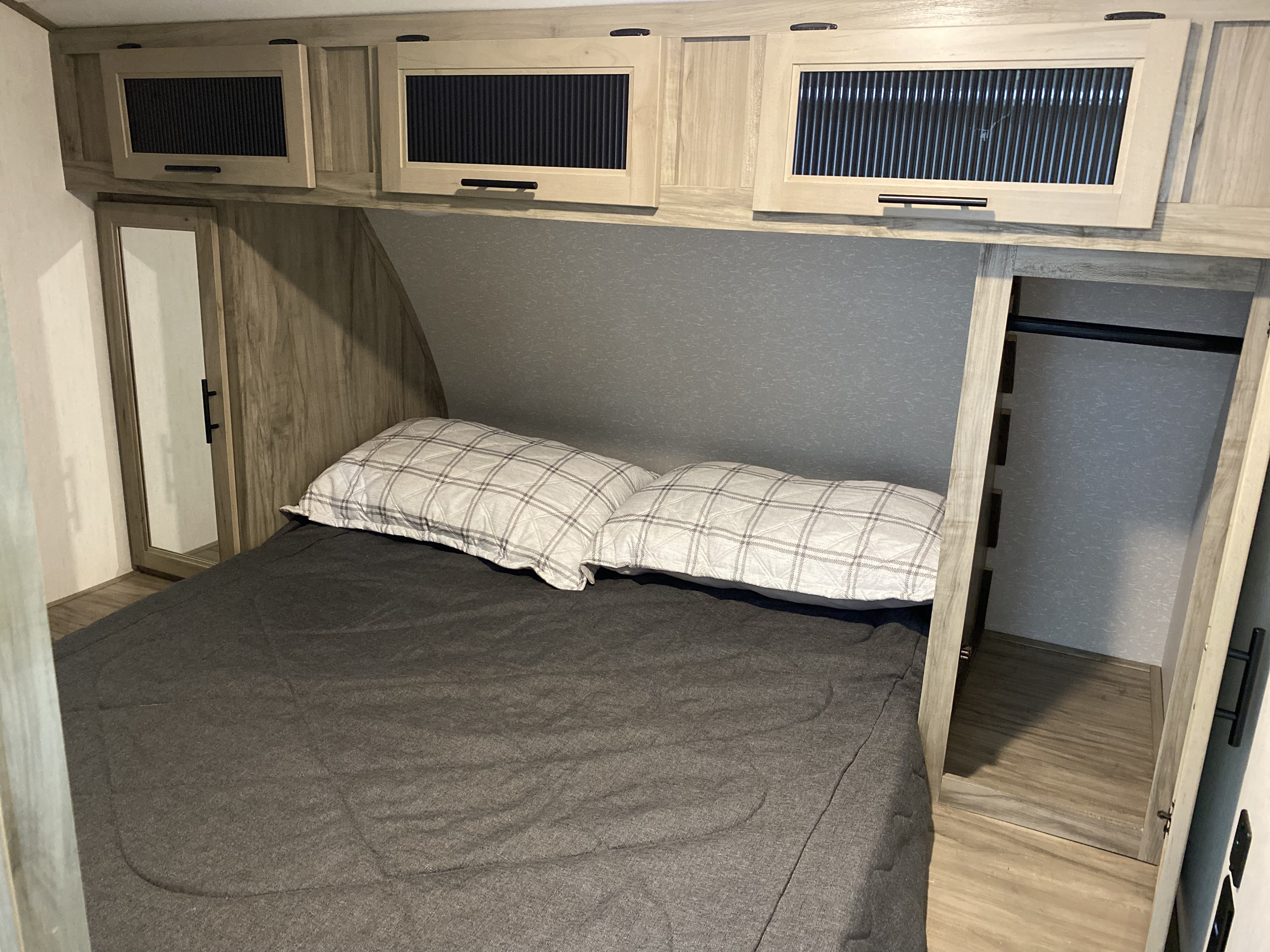 RV rental bedroom: light wood overhead cabinets, bed with plaid pillows, and open closet interior.. Forest River Cherokee Alpha Wolf 2022