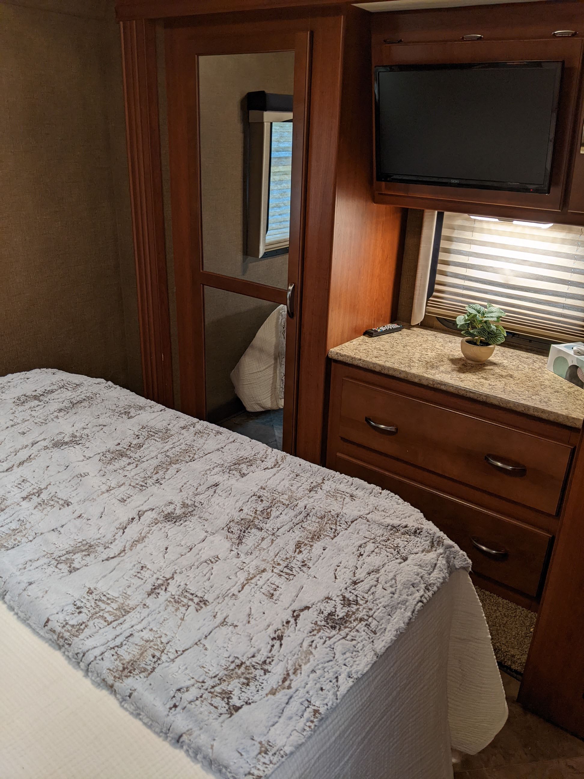 Cozy RV rental interior, featuring a bed with textured bedding, a mirrored closet, TV, and counter with storage drawers.. Thor ACE 30.2 2015