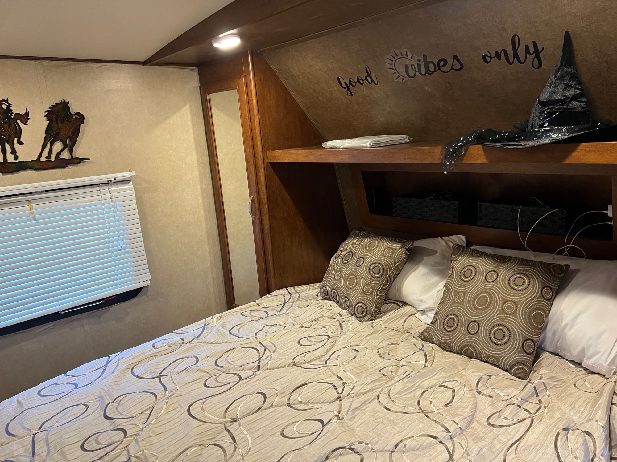 Cozy RV rental bedroom with a comfy bed, window, "good vibes only" wall art, and witch hat on shelf.. Forest River Vibe 2017