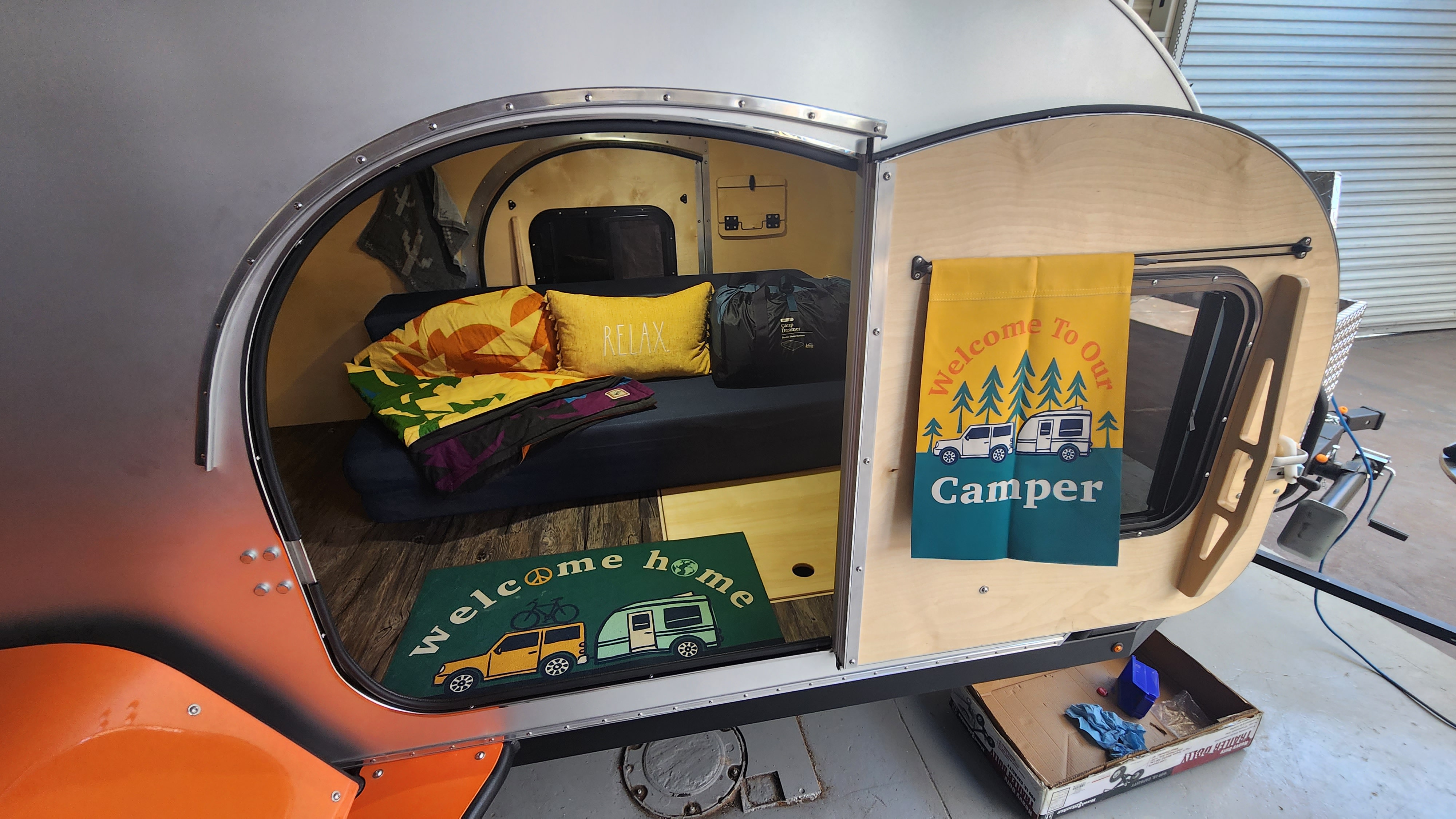 Teardrop camper interior viewed through open door. Cozy bed, "Relax" pillow, and welcome mat inside this RV rental.. SoCal Teardrop 511XS 2023