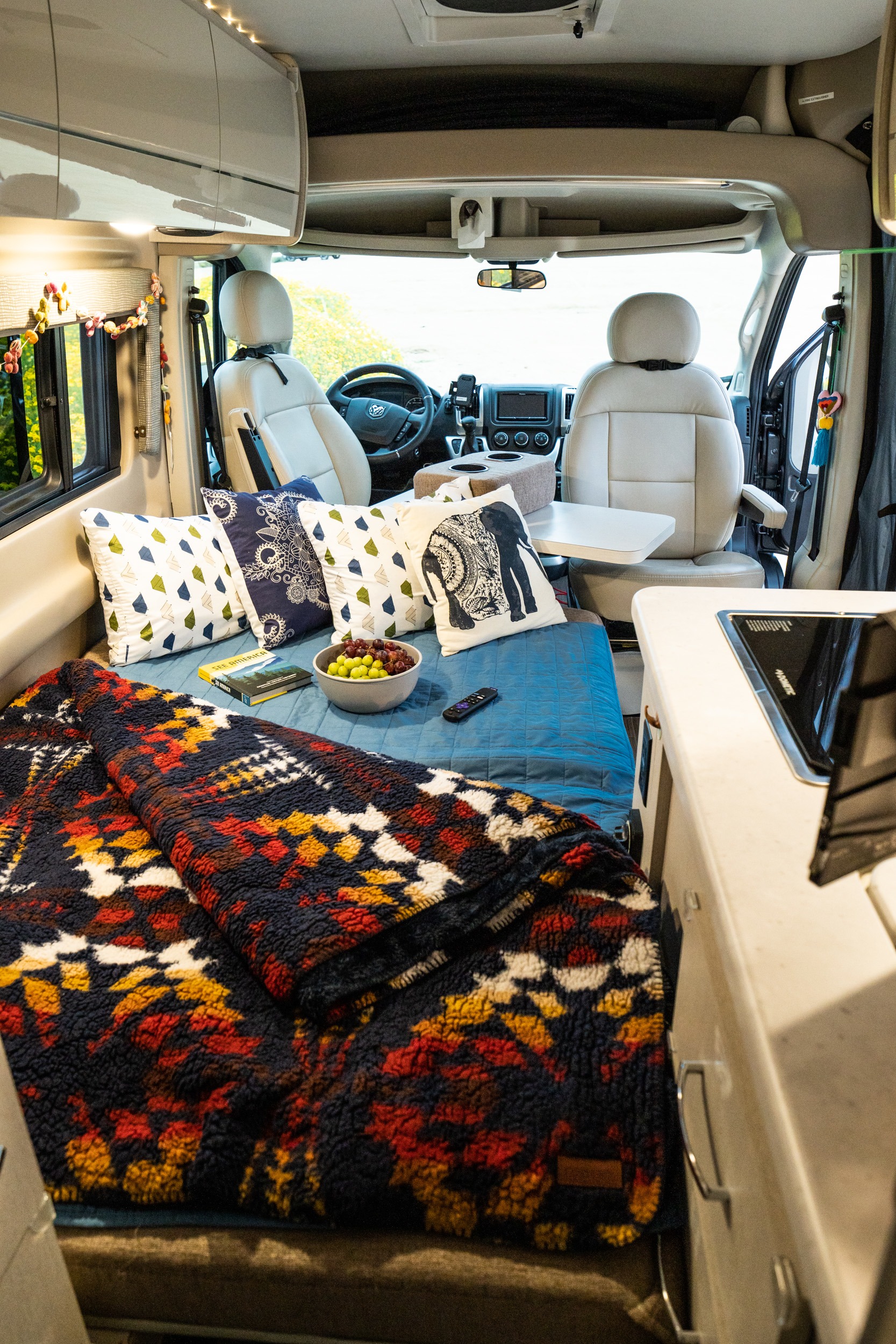 Step inside a comfortable RV rental: modern camper van interior with cozy bed, stylish pillows, and front cabin access.. Thor Rize 18M 2022