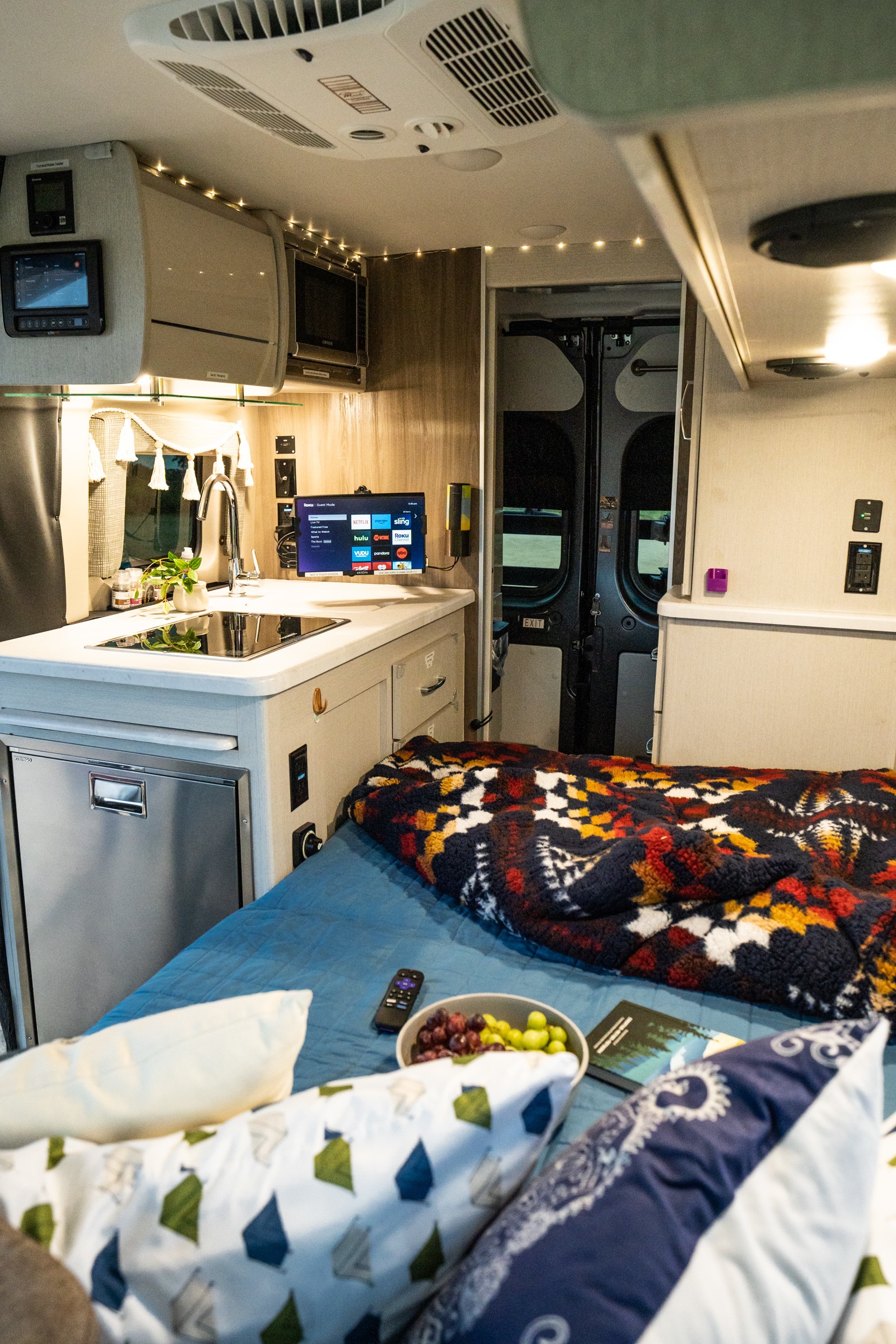 Explore a comfortable RV rental interior: kitchen, cozy bed with blanket, TV for entertainment, and overhead amenities.. Thor Rize 18M 2022