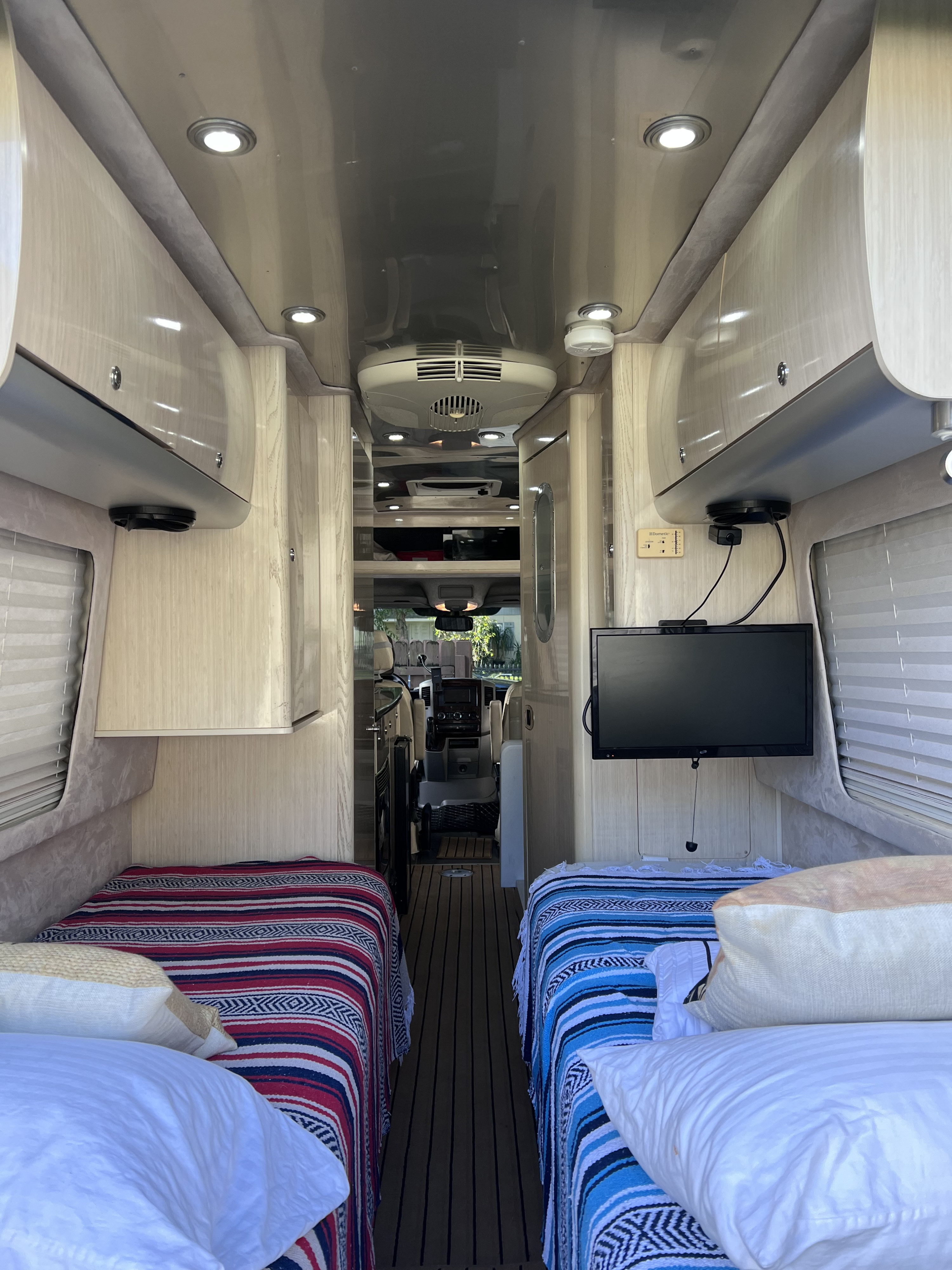 Inside an RV rental: cozy twin beds, overhead cabinets, and a TV, looking towards the cockpit.. Airstream Interstate 2012
