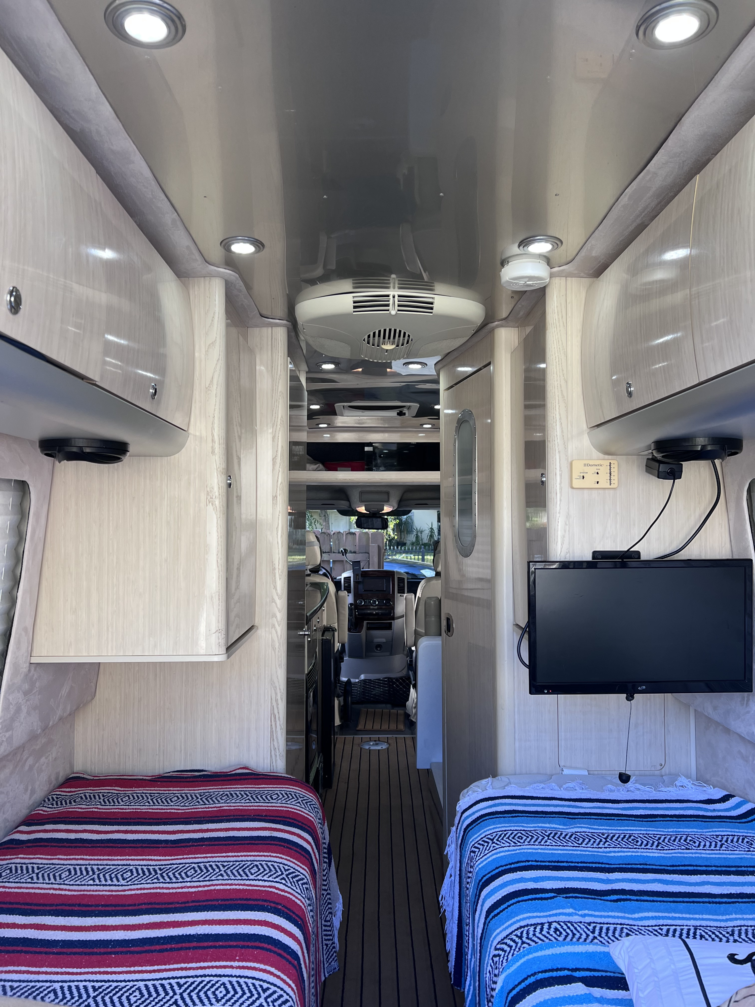 RV rental interior: A bright, modern compact living space with twin beds, overhead cabinets, and a view to the cockpit.. Airstream Interstate 2012