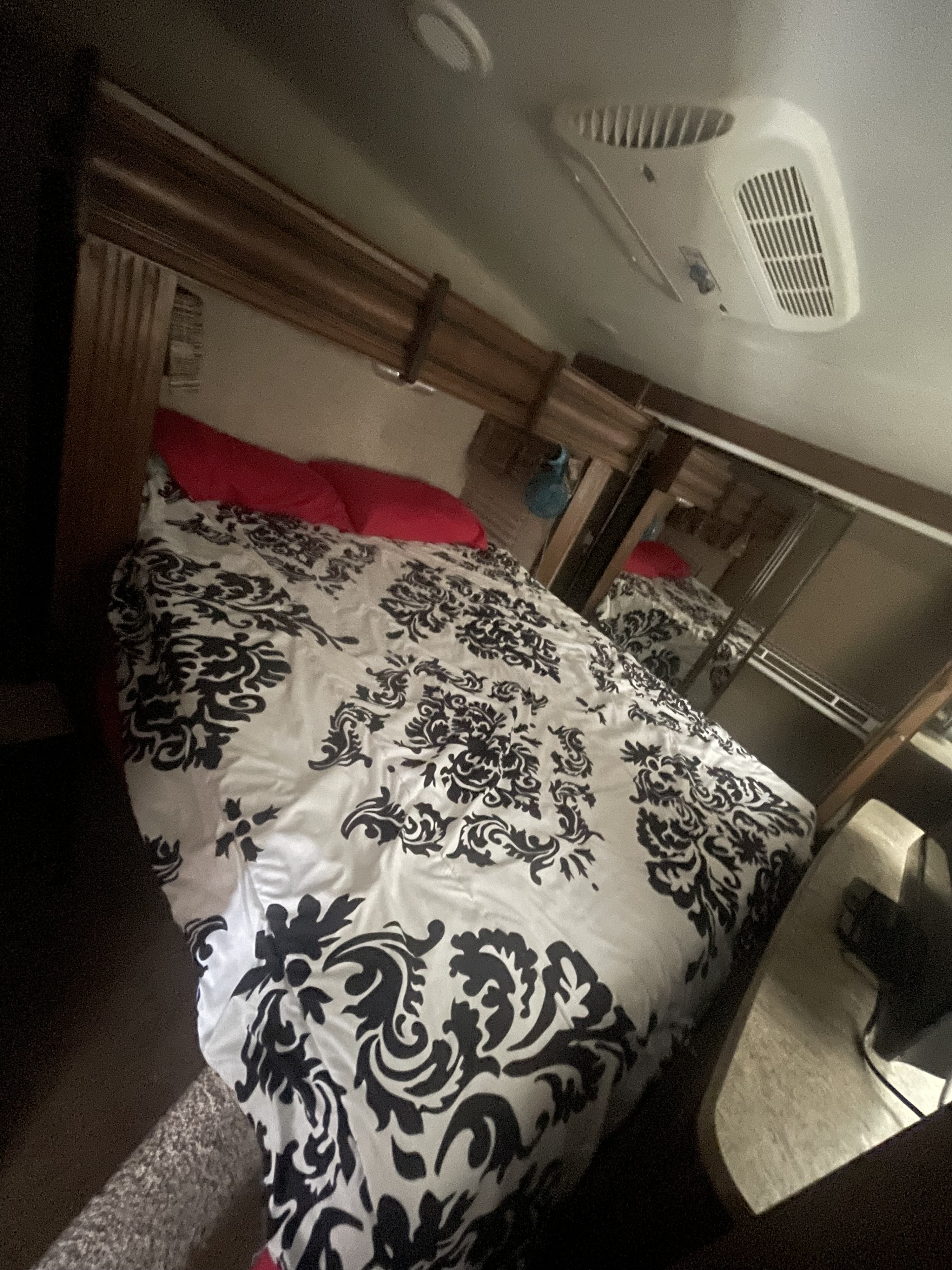 Cozy RV rental bedroom featuring a bed with a black and white damask comforter, red pillows, and ceiling AC unit.. Keystone RV Sprinter 2016