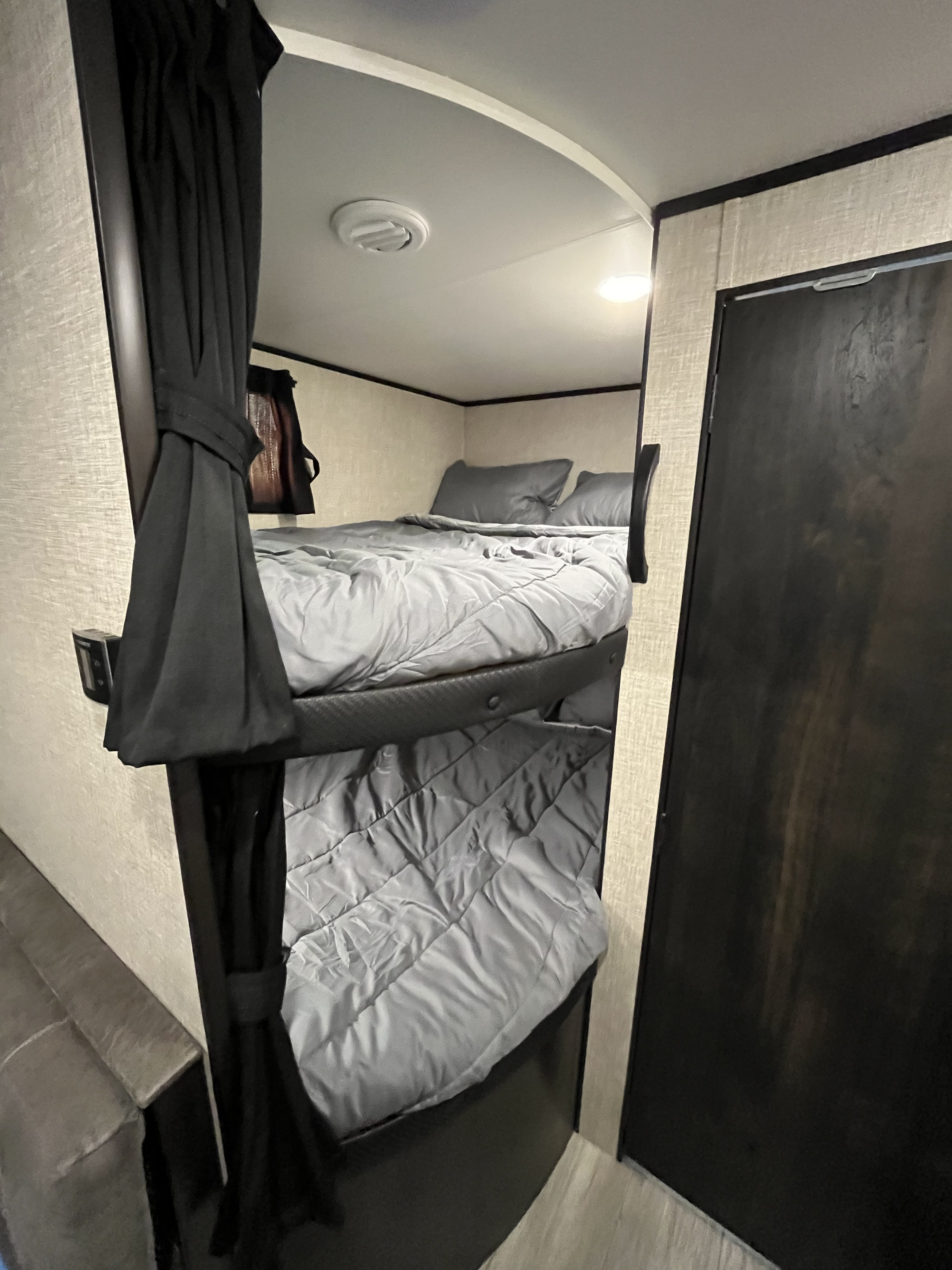 Inside an RV rental: Comfortable bunk beds with gray bedding and privacy curtains, ideal for compact sleeping.. Jayco Jay Flight 2022
