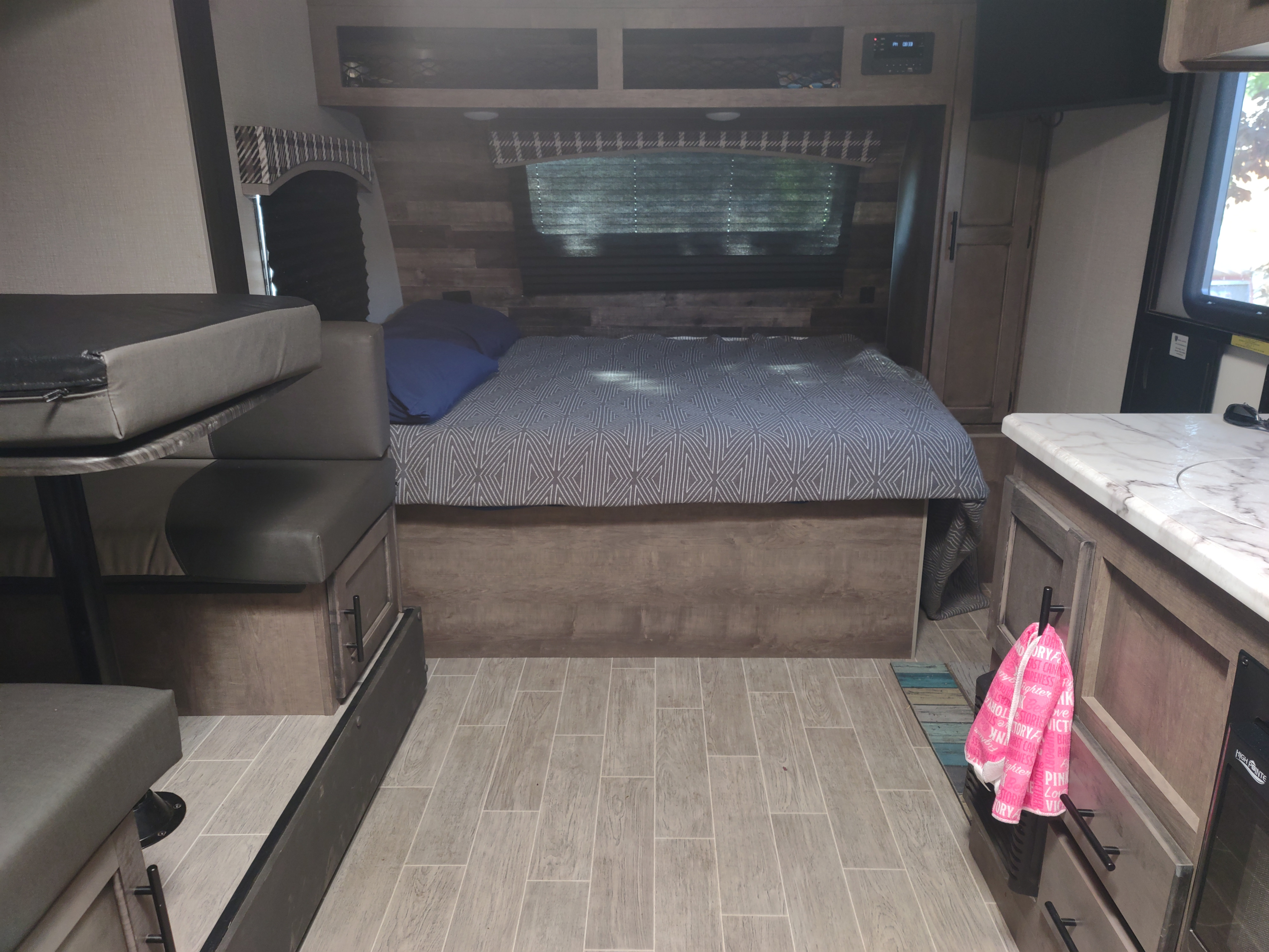 Interior view of an RV rental, featuring a comfortable bed, dinette, and kitchen space with light wood tones.. Sonic Lite 2021