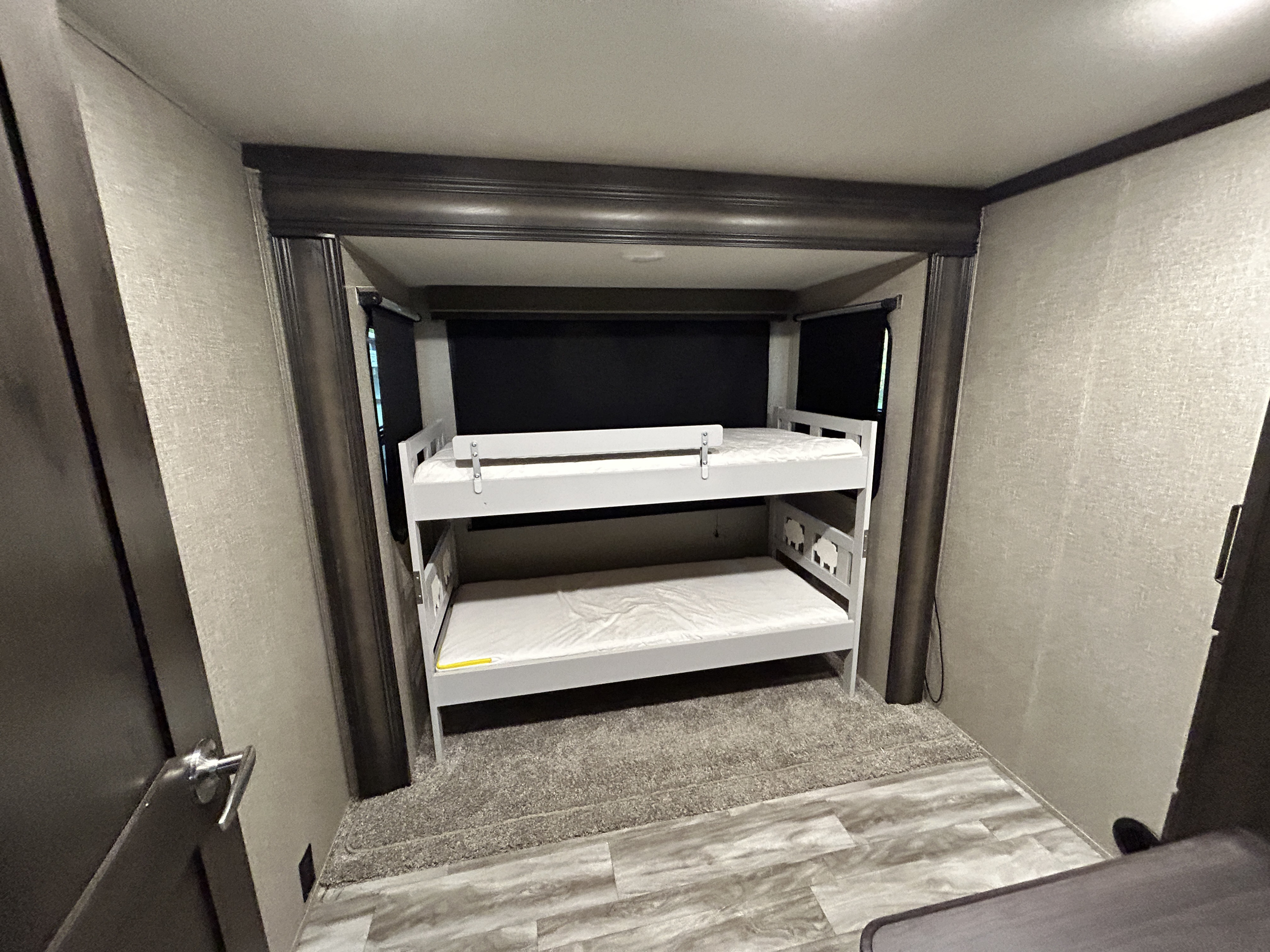 White bunk beds with mattresses inside an RV rental, featuring dark window shades. The floor is a mix of wood and carpet.. Grand Design Reflection 2022