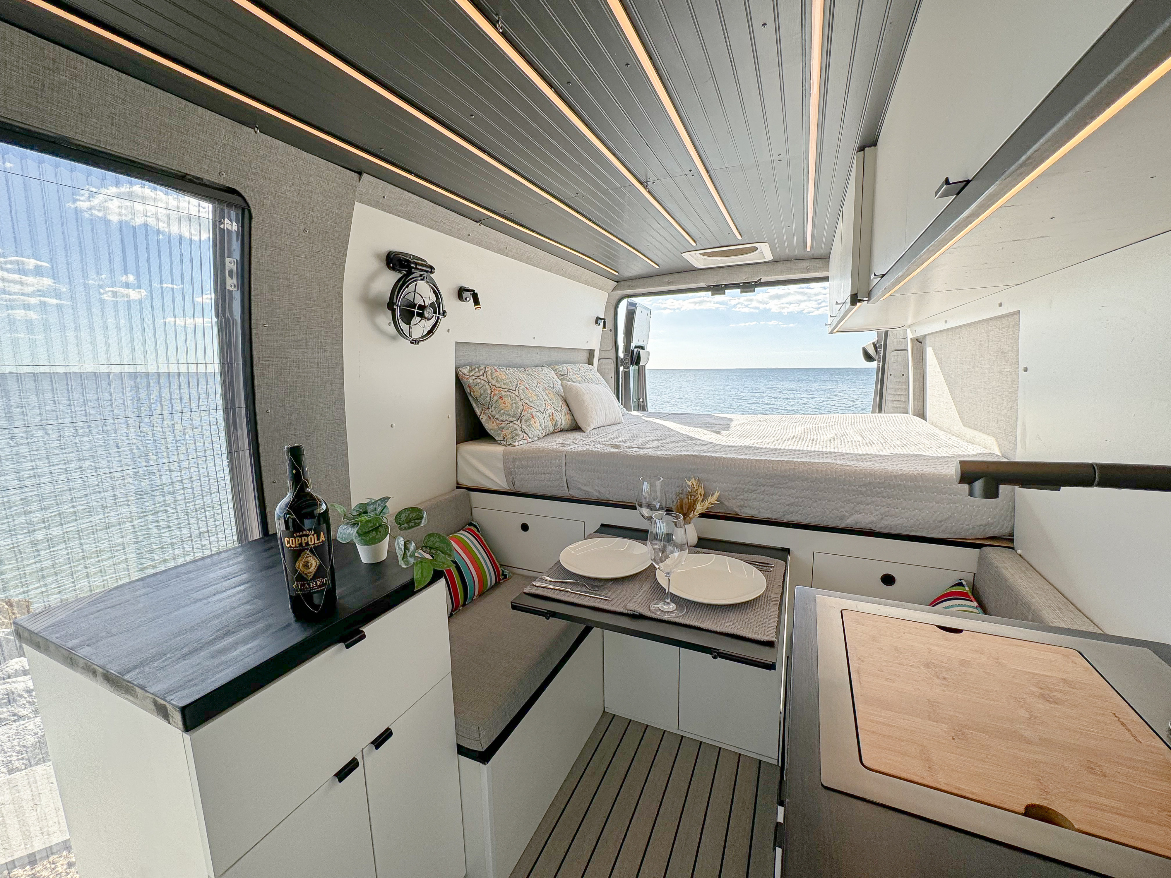 Spacious RV rental camper van interior with ocean view, comfortable bed, dining area, and kitchen setup.. Custom Built Other 2021