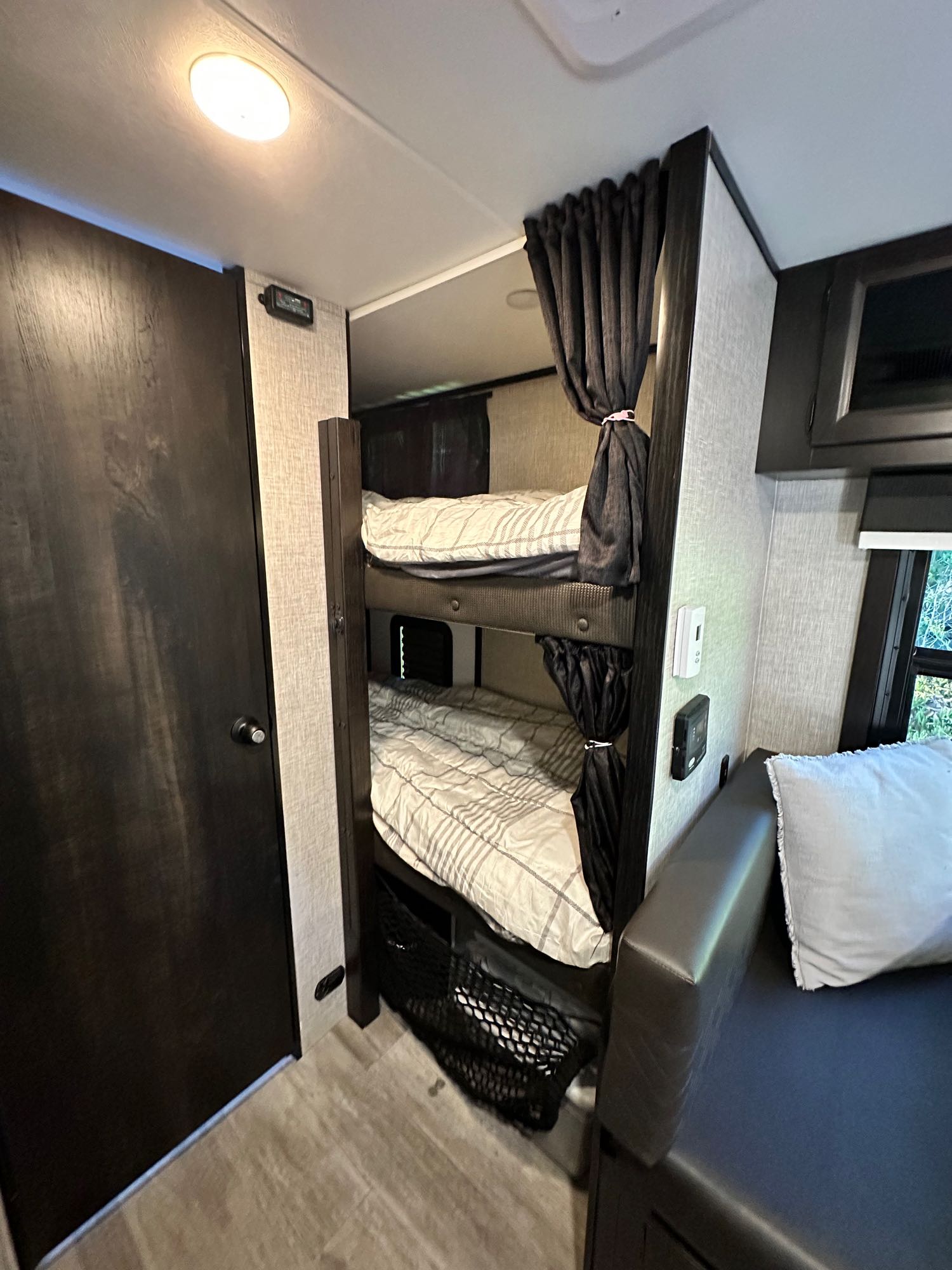 Cozy RV rental interior features dark wood bunk beds with privacy curtains, a door, and lounge seating.. Jayco Jay Feather Micro 2023