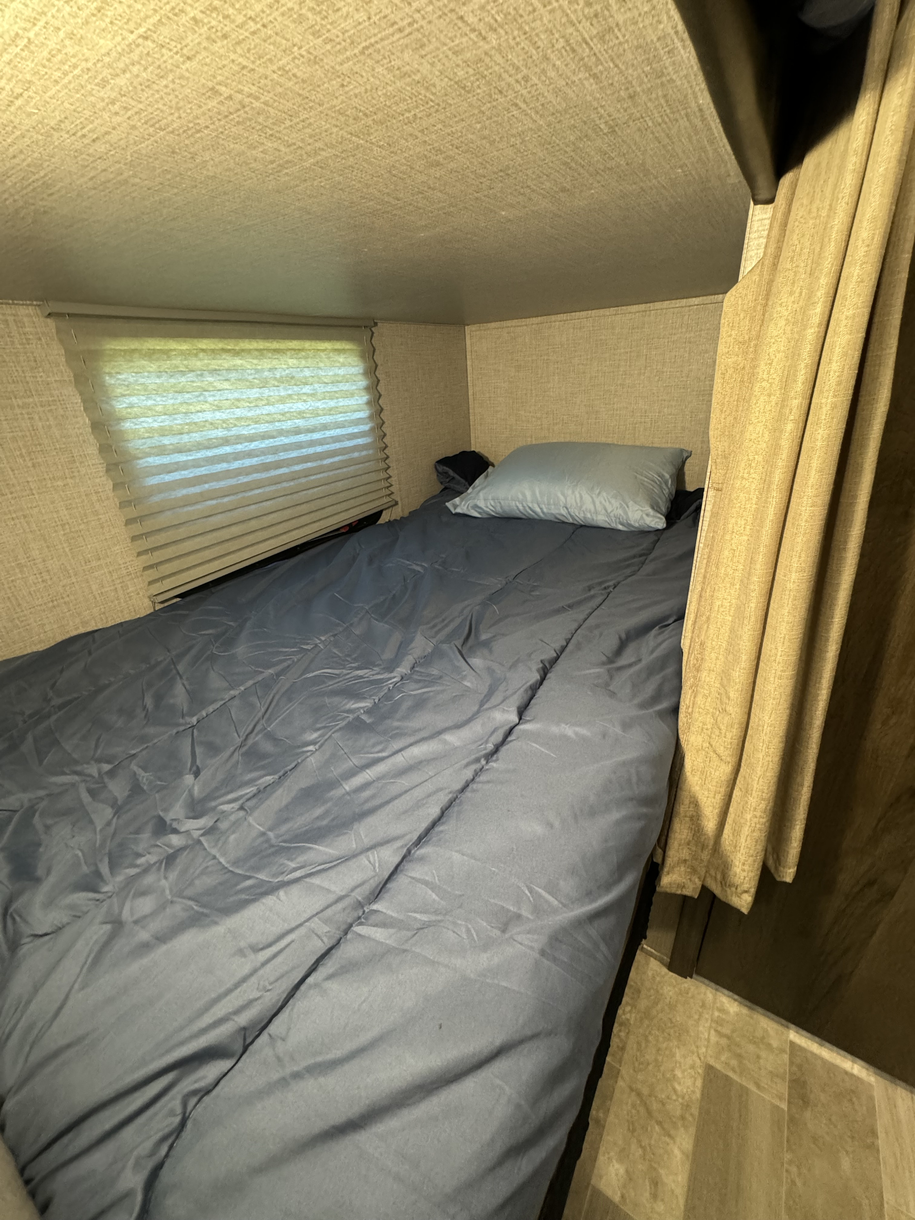 Cozy RV rental sleeping nook with a blue bed, window blinds, and privacy curtains.. East to West Della Terra 2021