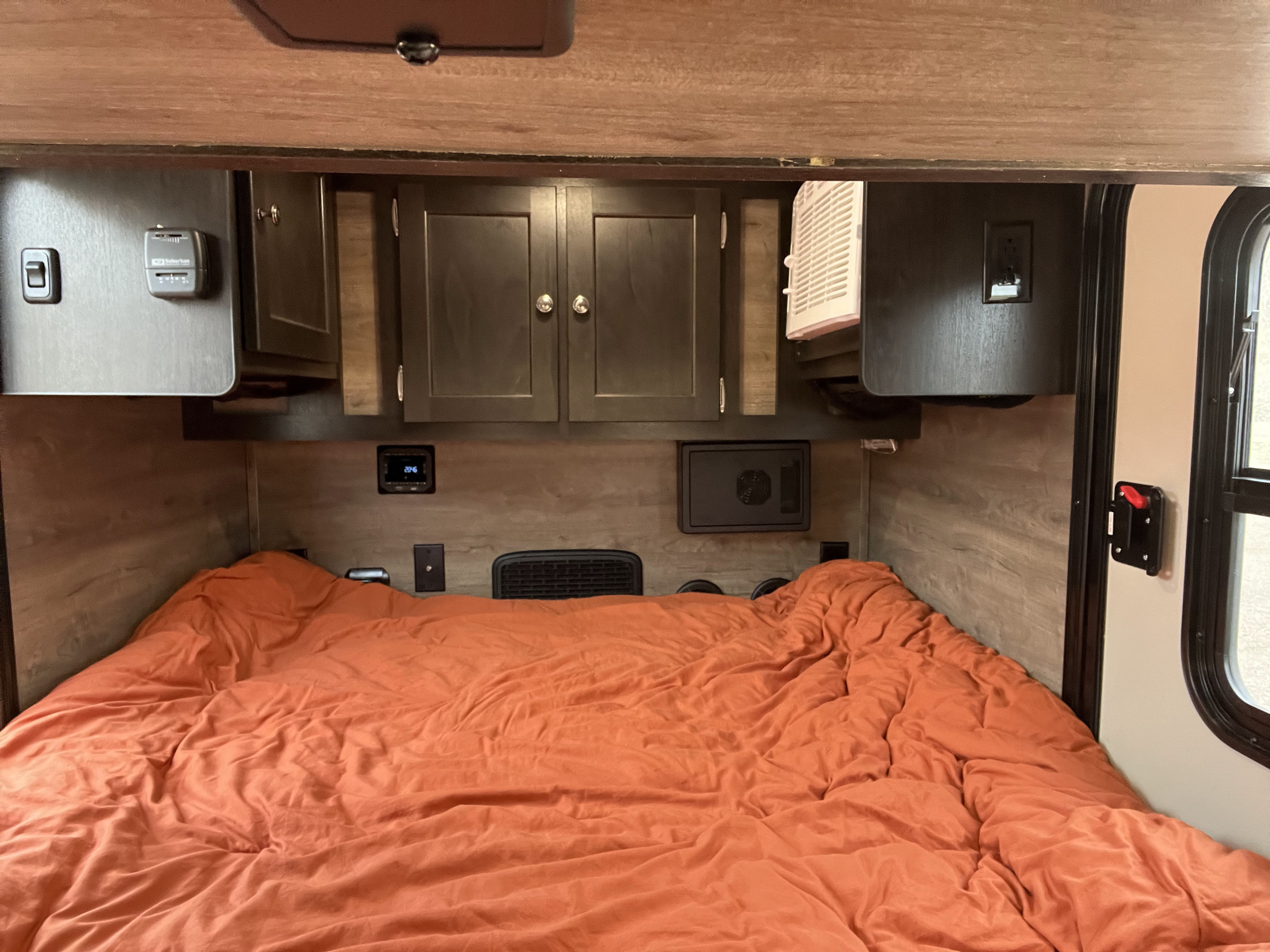 Cozy RV rental bedroom with an orange bed, dark wood cabinets, thermostat, power outlets, and a window.. Braxton Creek Free Solo 2022