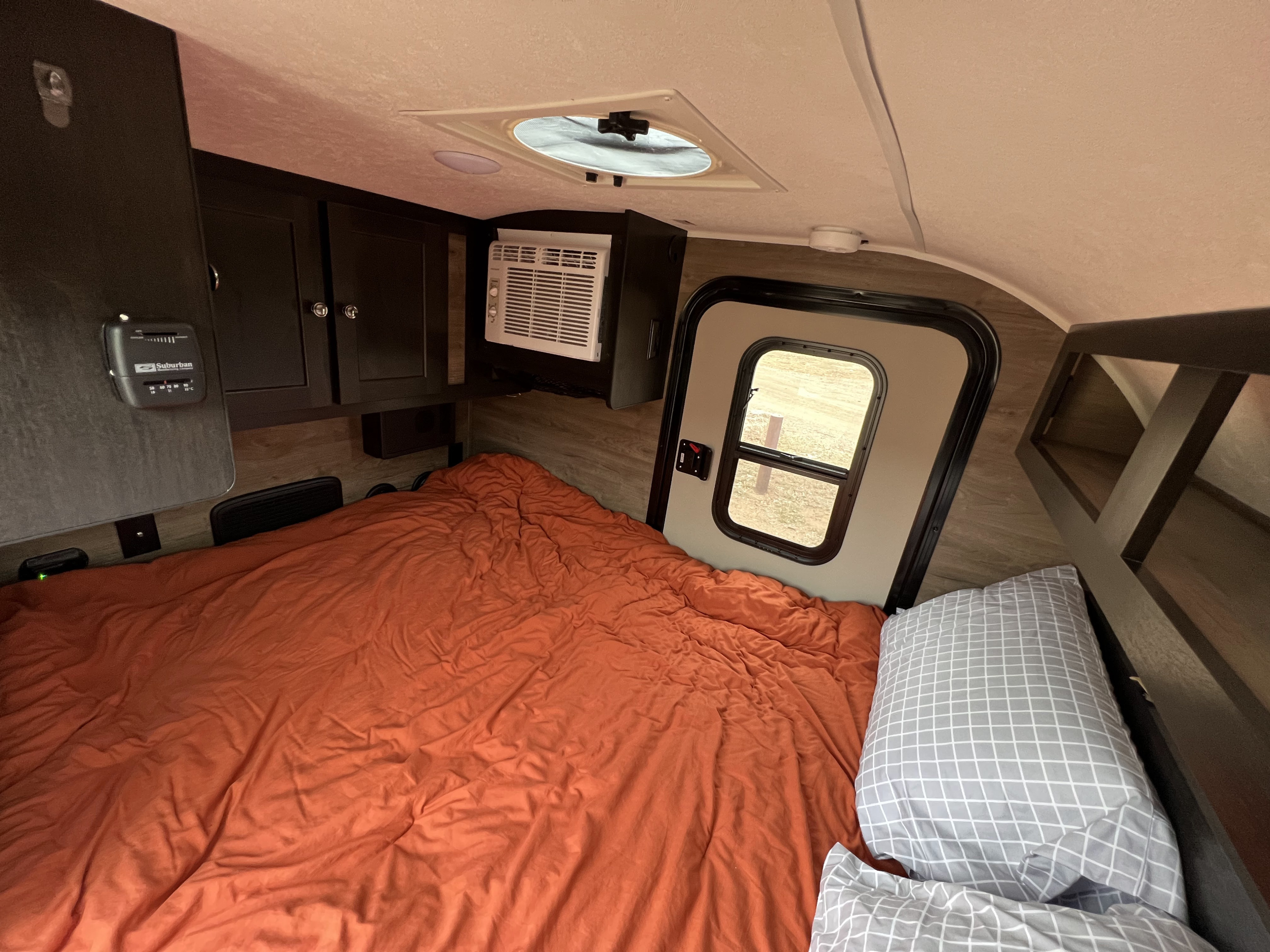 This rv rental shows a cozy bedroom with an orange bed, AC unit, thermostat, and storage, perfect for your next trip.. Braxton Creek Free Solo 2022