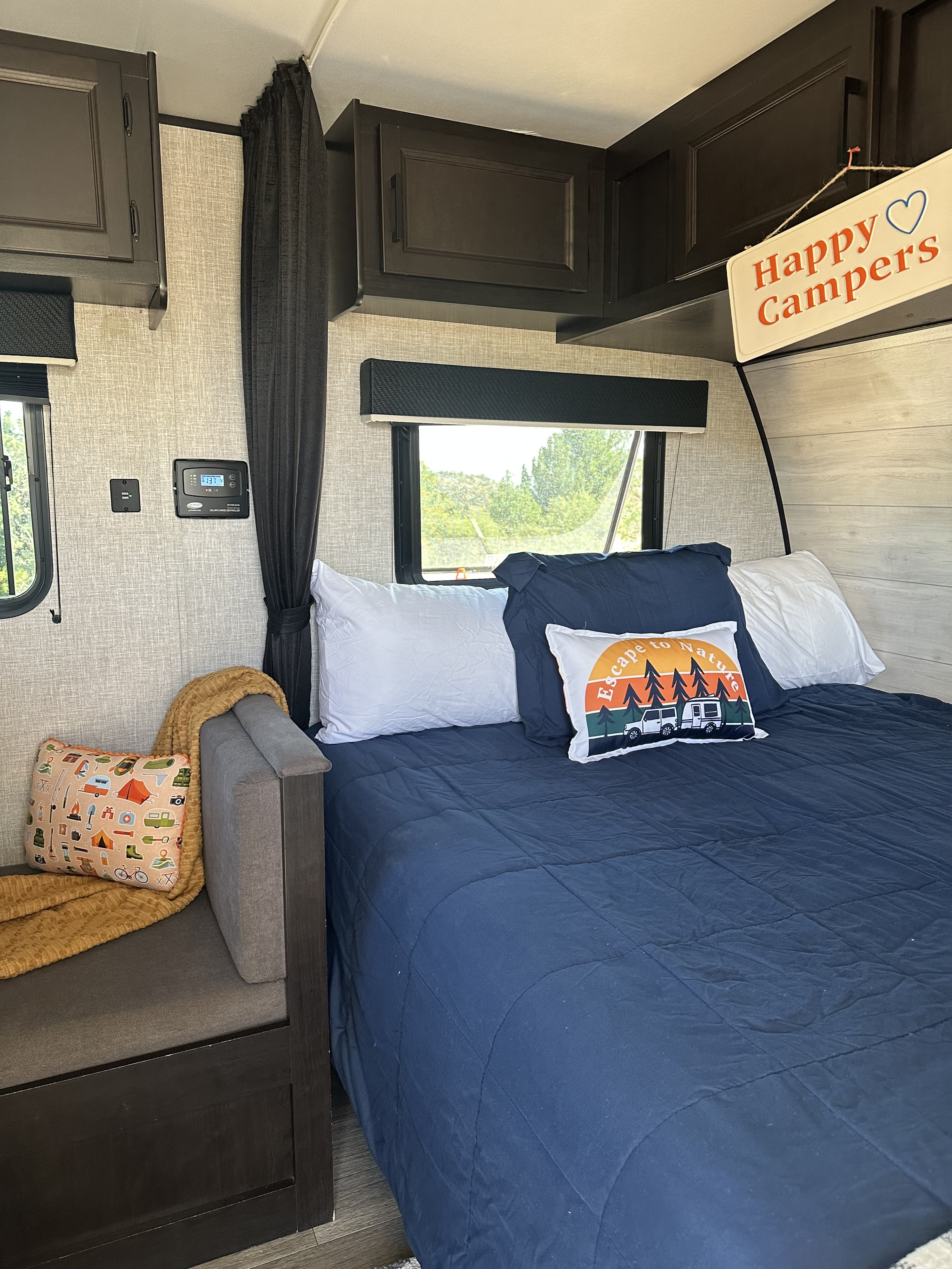 Cozy RV rental bedroom with comfy bed, camping pillows, natural views, & "Happy Campers" sign.. Jayco Jay Flight SLX 2023