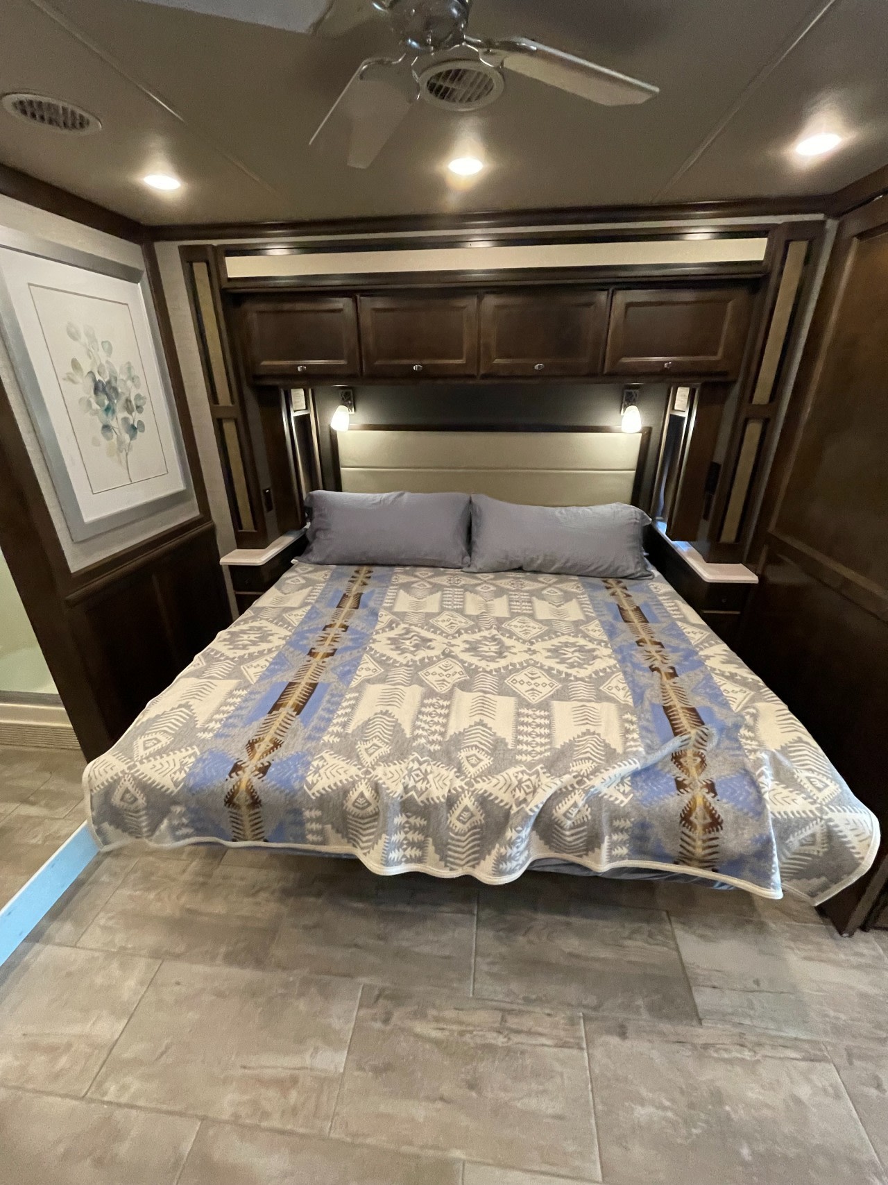 Inside an **rv rental**, a well-appointed bedroom with a patterned blanket on the bed, overhead cabinets, and a ceiling fan.. Tiffin Motorhomes Allegro Red 2020