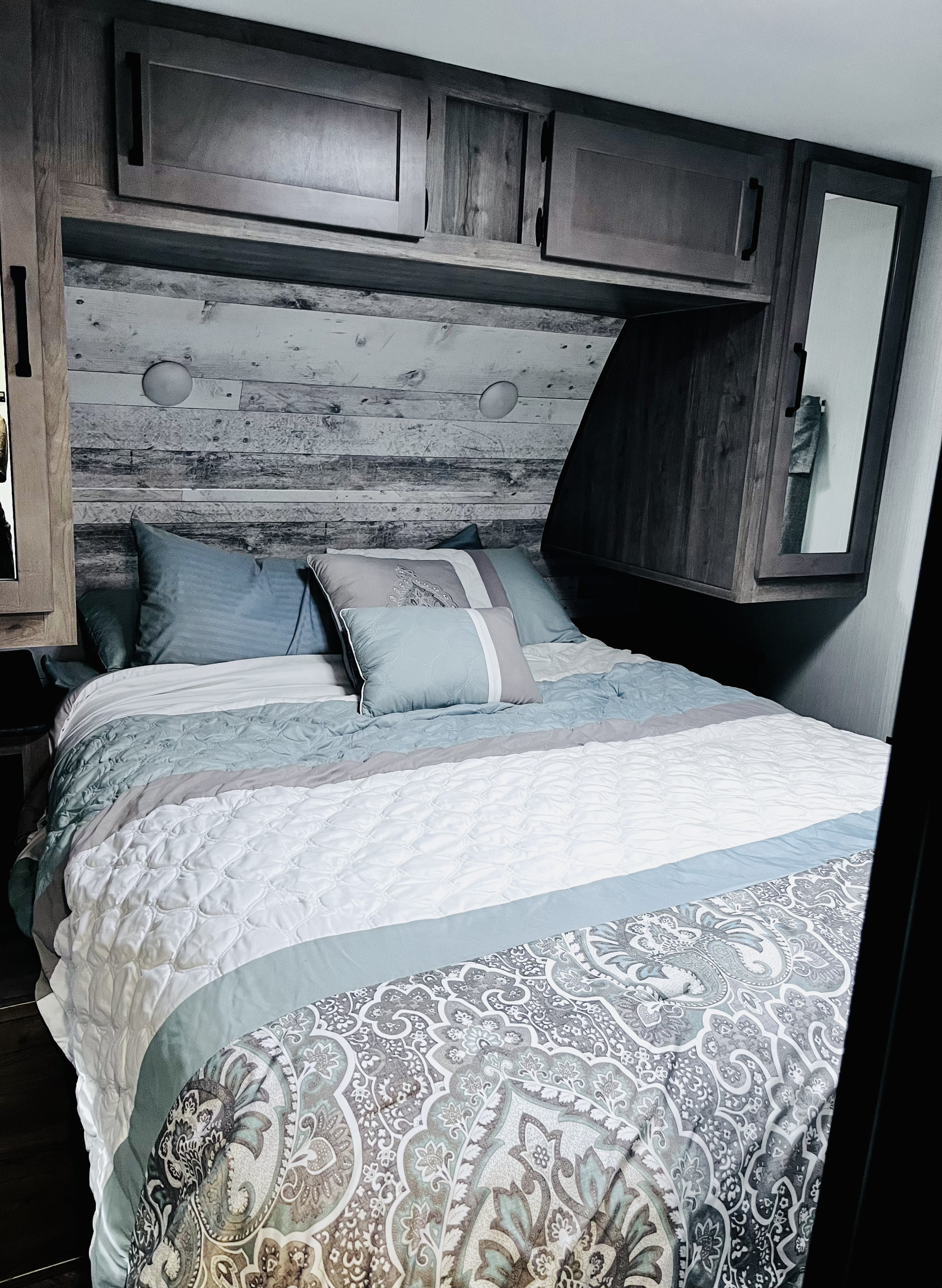 Inside an RV rental: a comfy bedroom with soft blue & grey bedding, shiplap headboard, and built-in overhead cabinets.. Forest River Puma 28bhss 2024