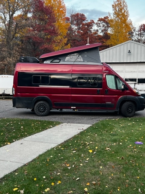 Maroon pop-top camper van, ideal for RV rental getaways. Fall trees frame this adventure vehicle.. Winnebago Solis 2021