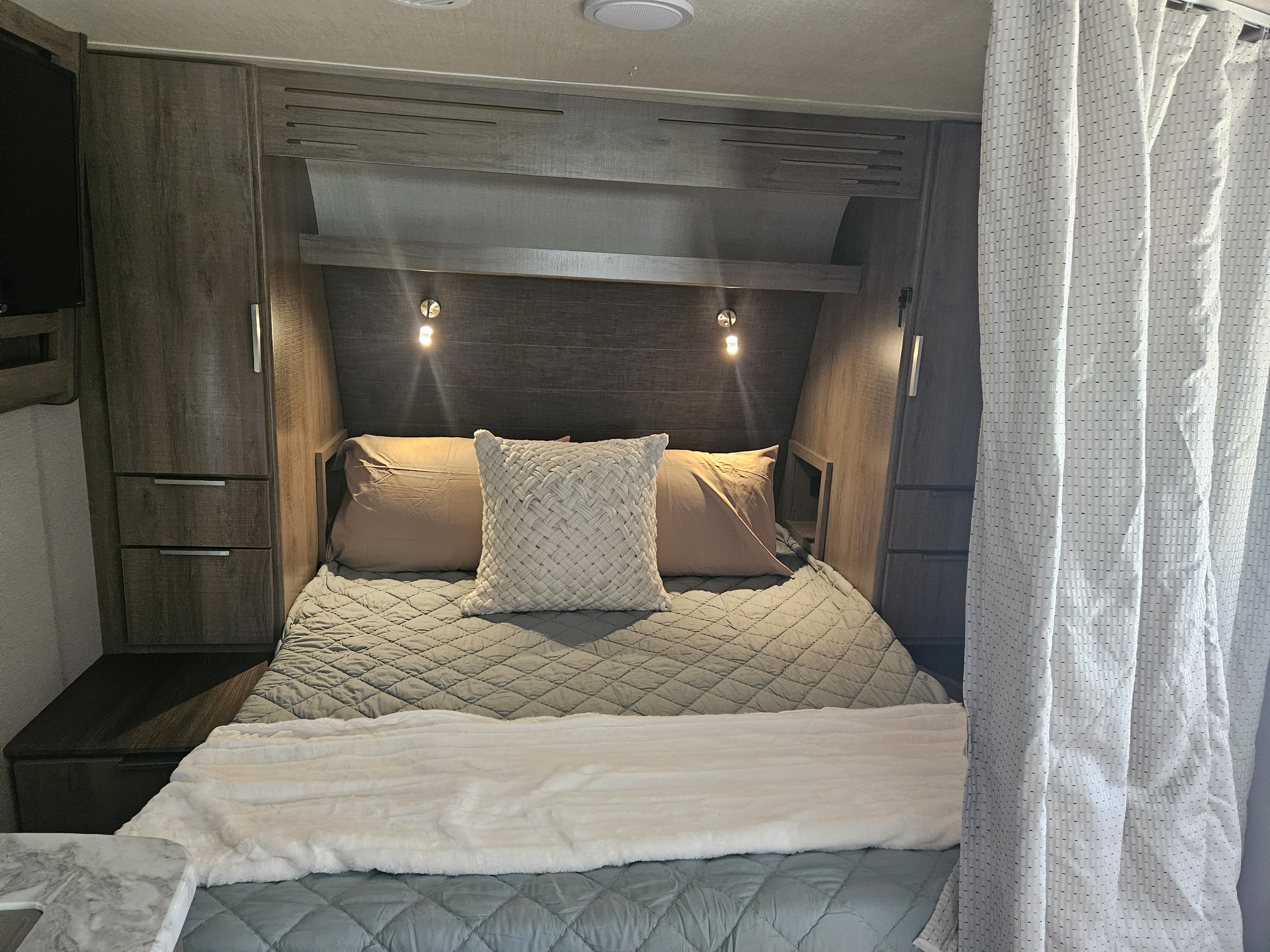 Cozy RV rental bedroom with a comfy bed, overhead storage, and integrated lighting, perfect for a relaxing getaway.. Grand Design Imagine XLS 2021