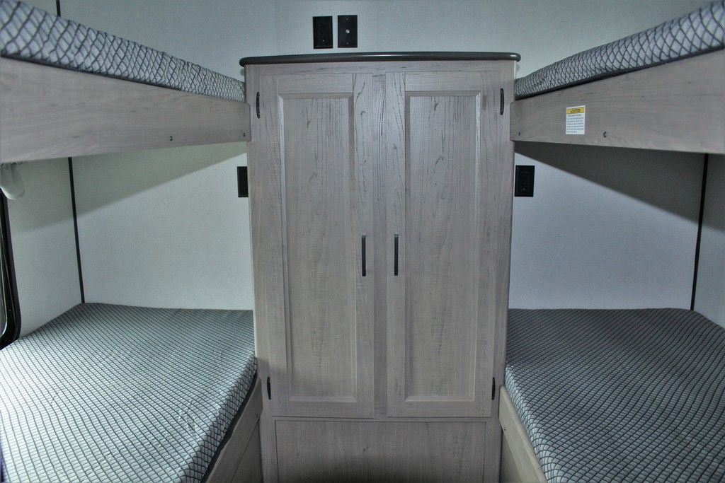 RV rental bunk beds (left & right) with a central wood wardrobe cabinet and wall outlets for charging.. Keystone RV Hideout 2021