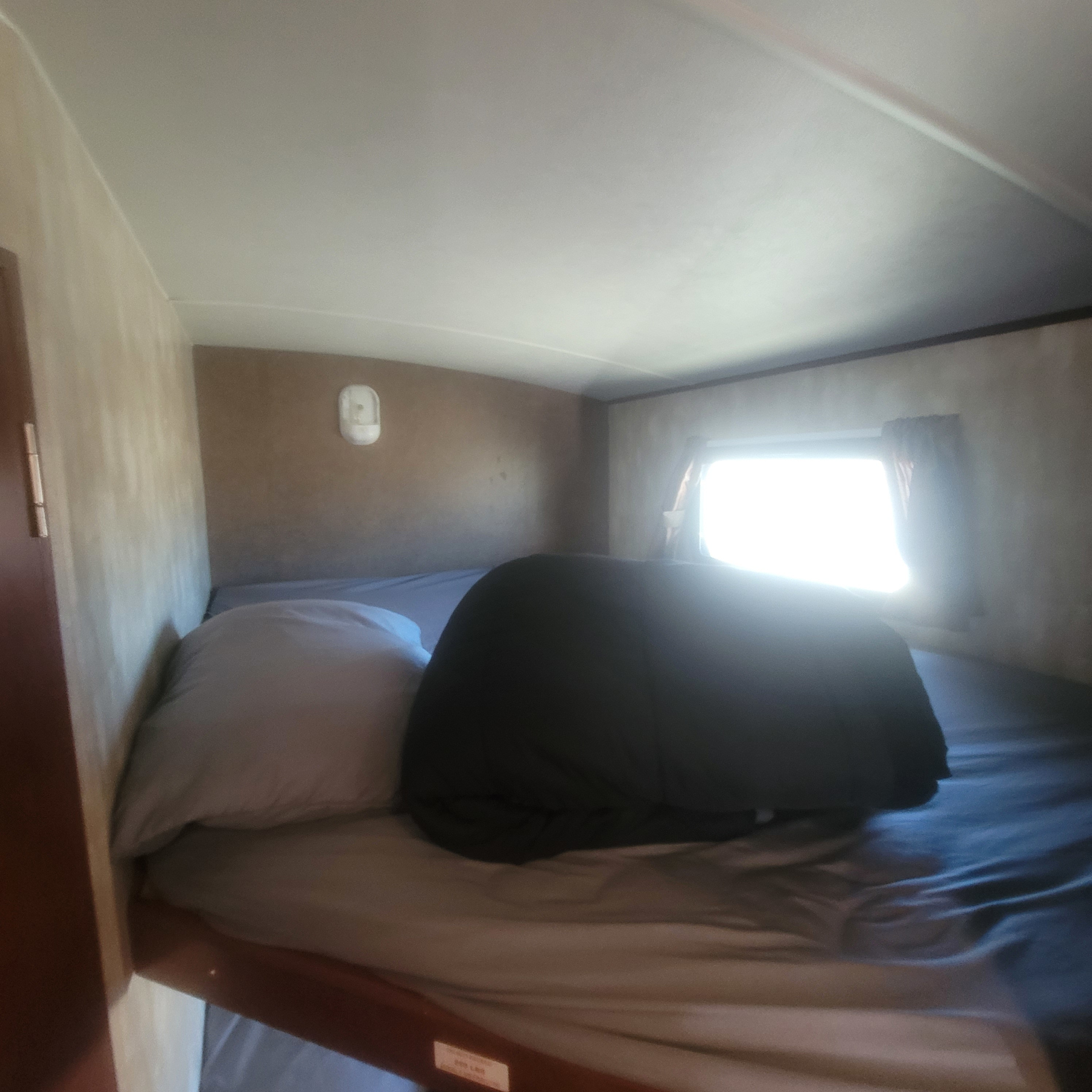 Inside an RV rental: a compact bunk bed area with a pillow, rolled dark blanket, and bright window. Ready for your adventure.. Winnebago Ultralite 2014
