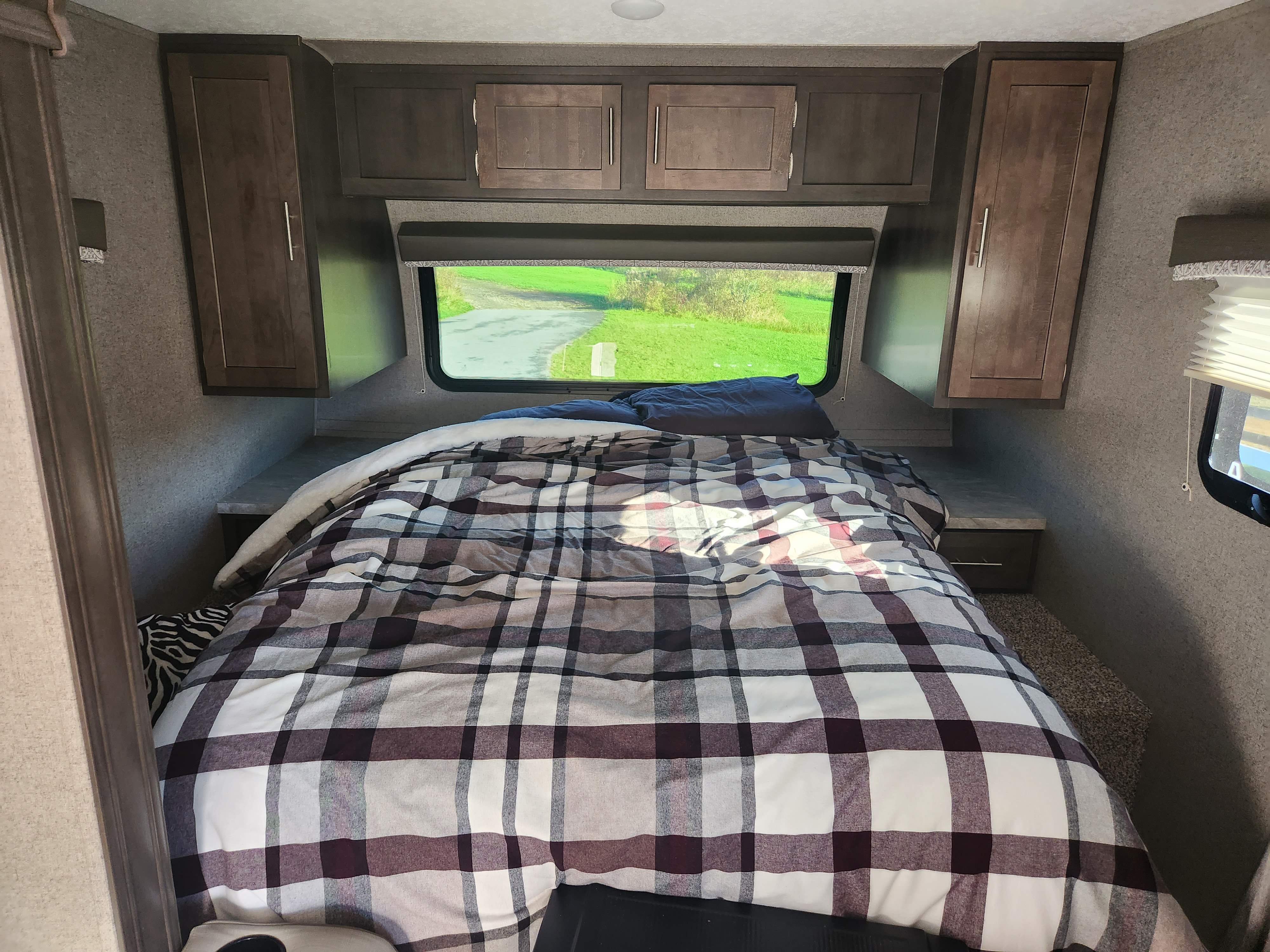 Cozy RV rental bedroom featuring plaid bedding, overhead cabinets, and a scenic window view. Ideal for travel trailer getaways.. Forest River Rockwood Mini Lite 2019