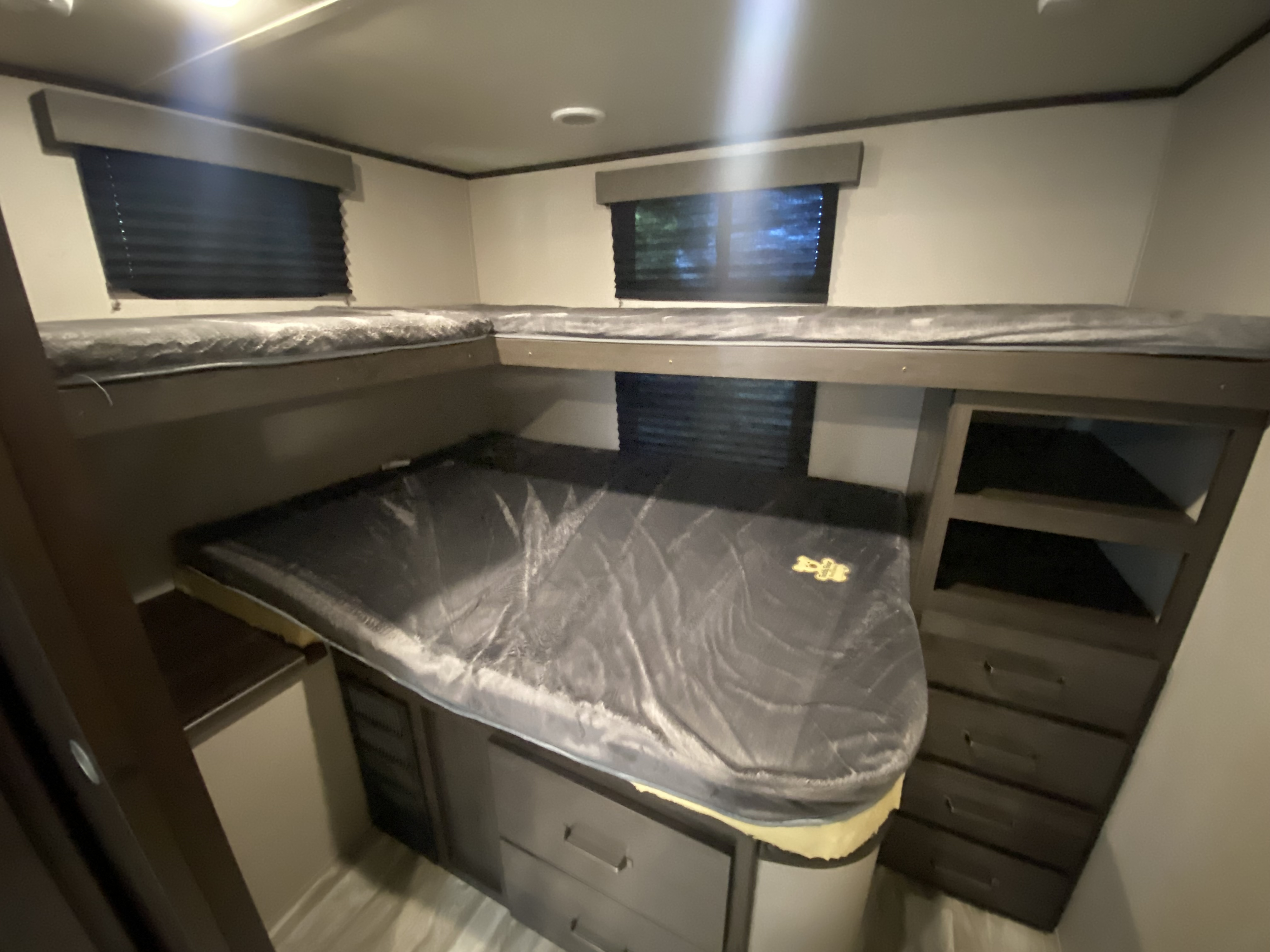RV rental interior featuring a comfortable L-shaped bunk bed with an upper bunk, privacy blinds, and built-in drawer storage.. Grand Design Transcend 2021
