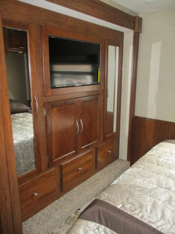 RV rental interior: cozy bedroom with built-in TV, ample wooden storage, and comfortable bedding.. Forest River Coachmen Pursuit 2017